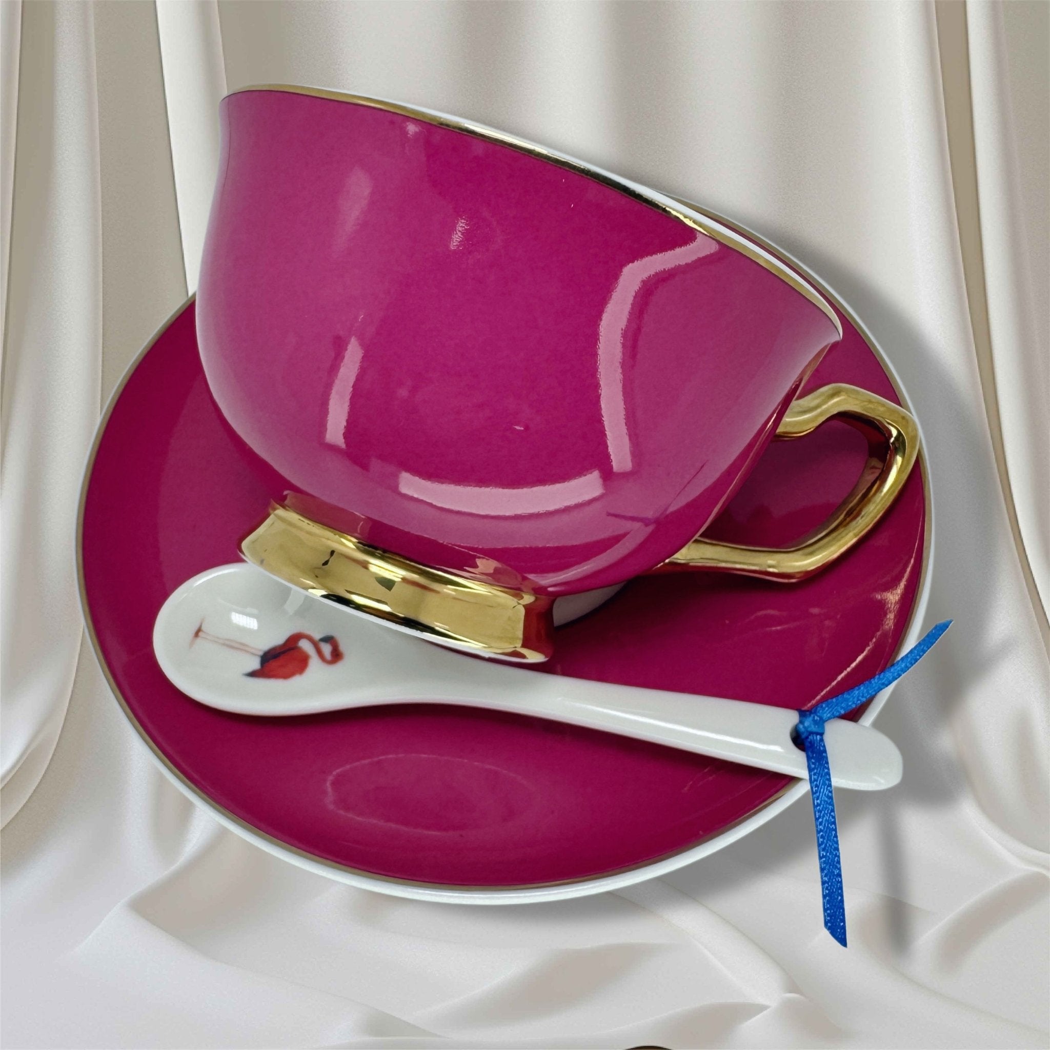 Magenta teacup with gold handle and Alice in Wonderland print on the exterior, sitting on a matching houndstooth saucer.