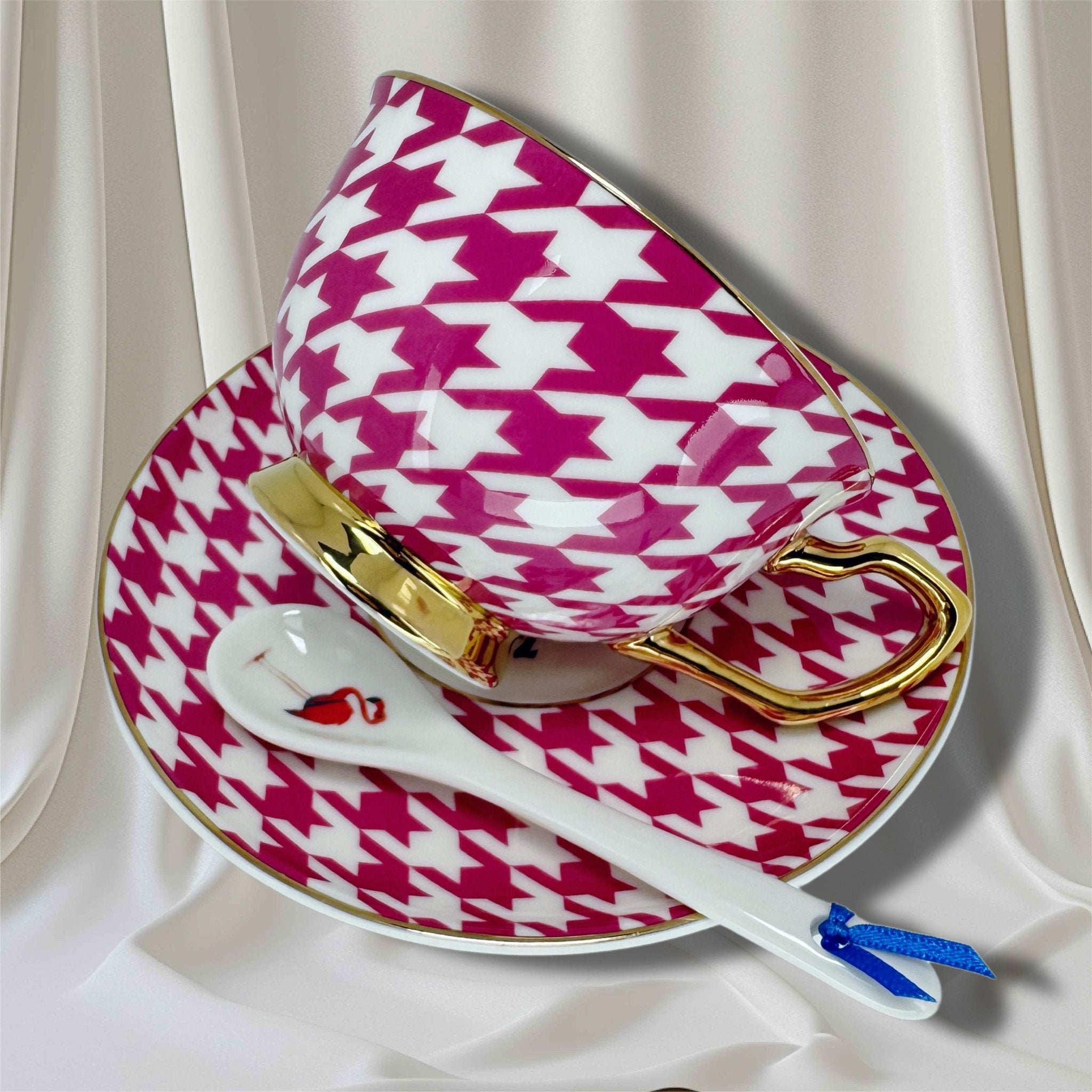 Pink and white houndstooth patterned teacup and saucer set with a spoon on a white background