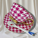 Pink and white houndstooth patterned teacup and saucer set with a spoon on a white background