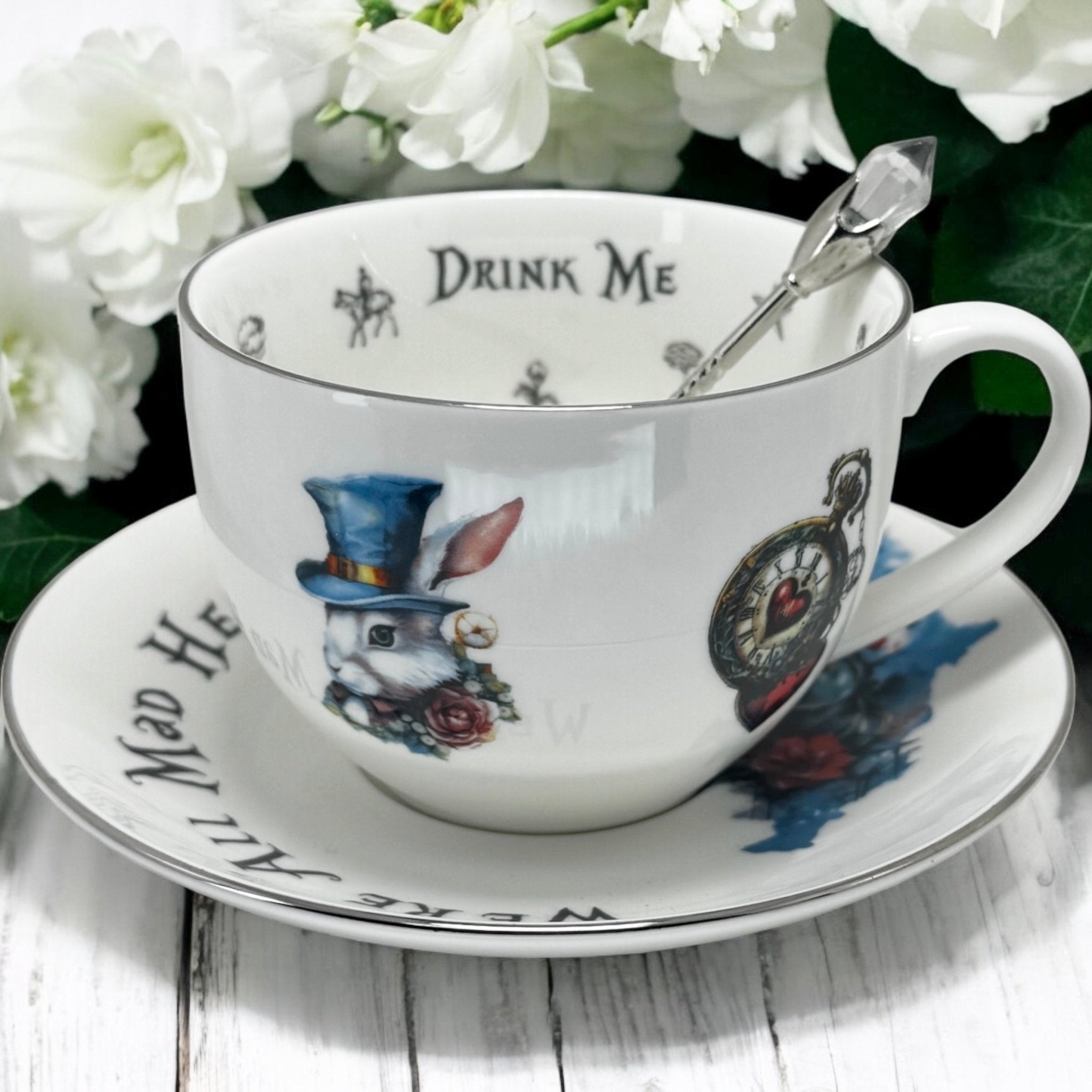 Teacup and saucer with rabbit illustration and 'Drink Me' text, surrounded by white flowers.