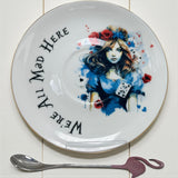 Decorative plate with a artistic design of a woman and text 'We're All Mad Here' on a white background.