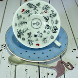 Side view of the blue polka dot teacup tilted on the saucer, showing the internal black and white illustrations of Alice in Wonderland characters