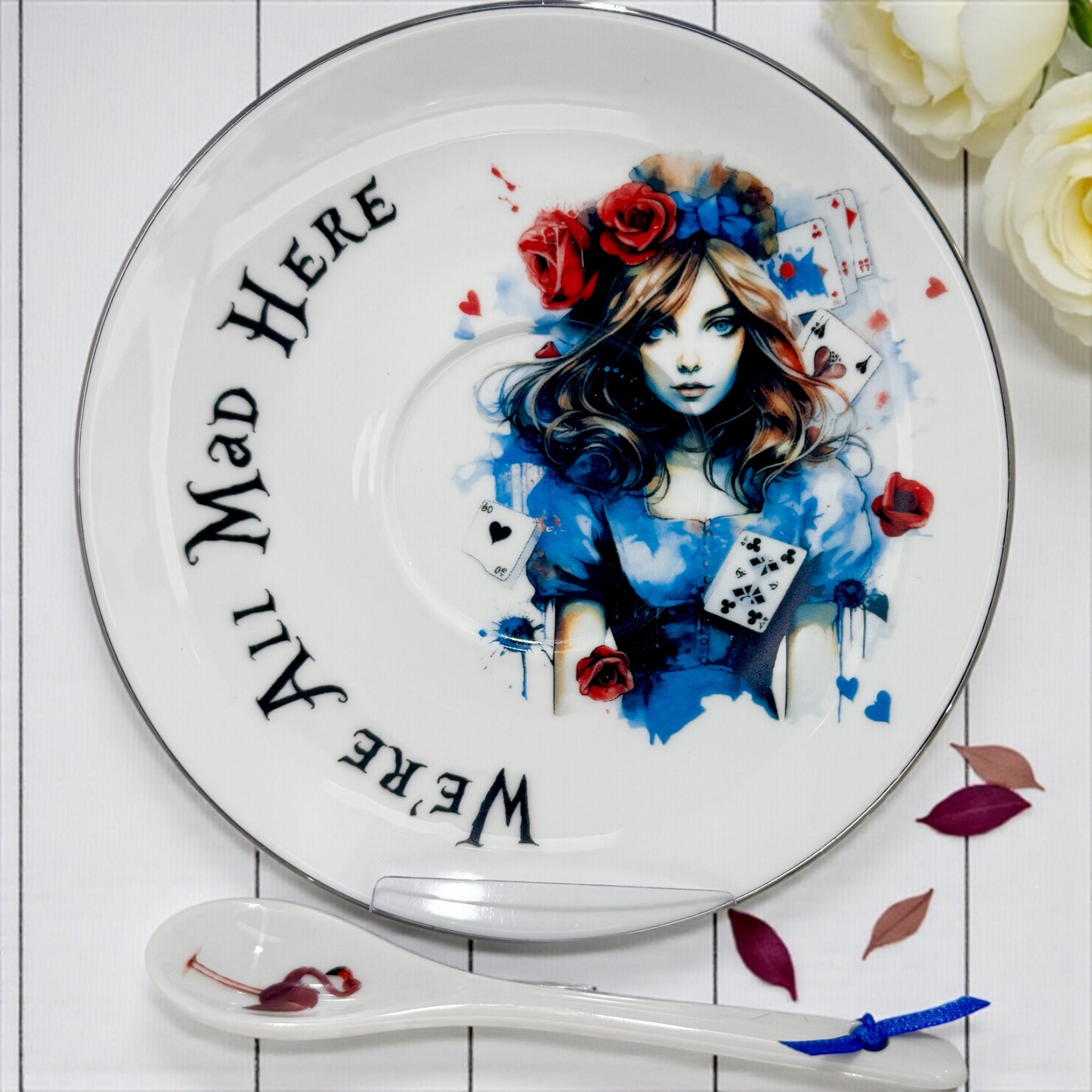 Overhead shot of the Saucer, featuring the Alice Queen of Hearts portrait, 'We're All Mad Here' text, and flamingo spoon