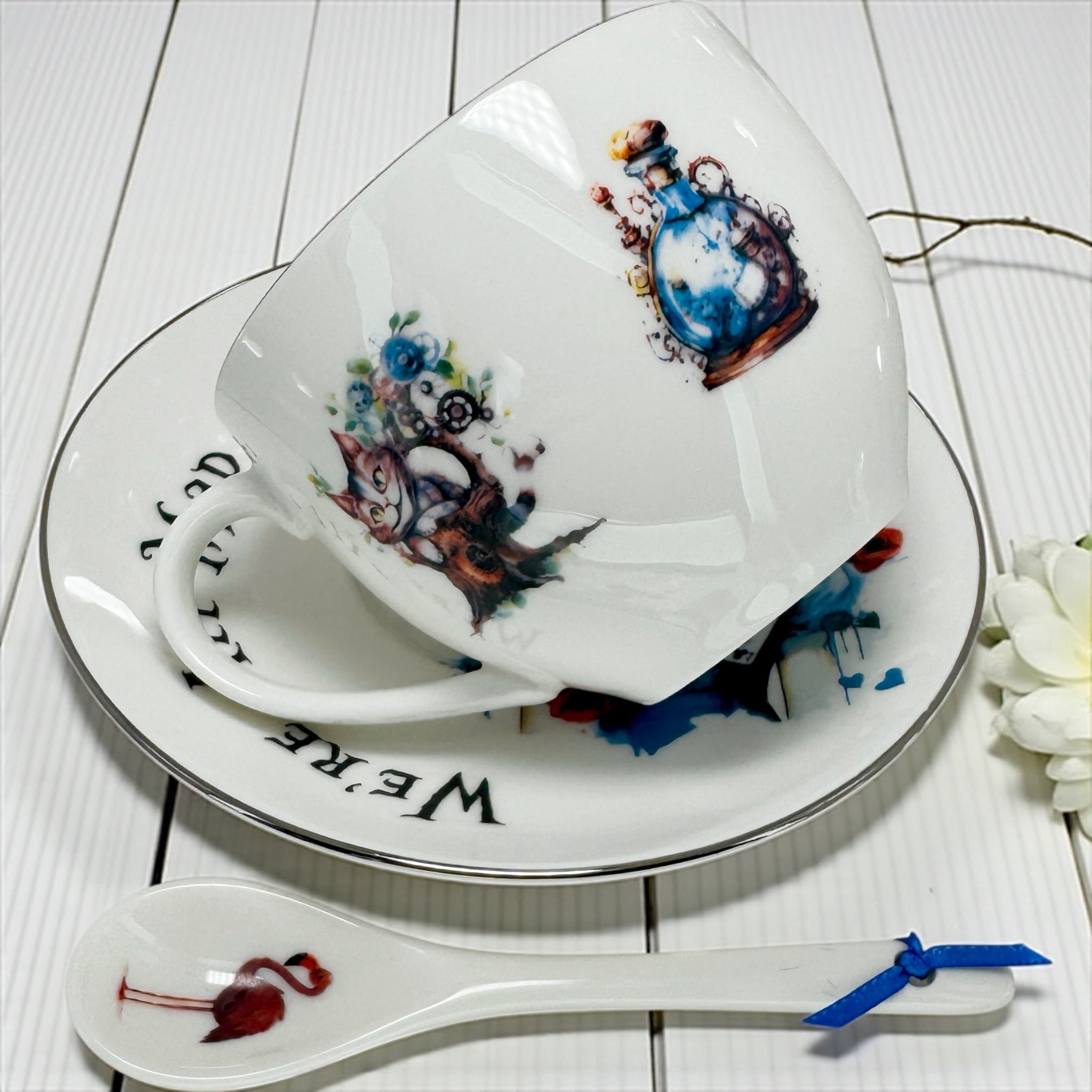 Tilted view of the Teacup showing the 'Drink Me' Potion Bottle and Cheshire Cat artwork, silver rim detailing