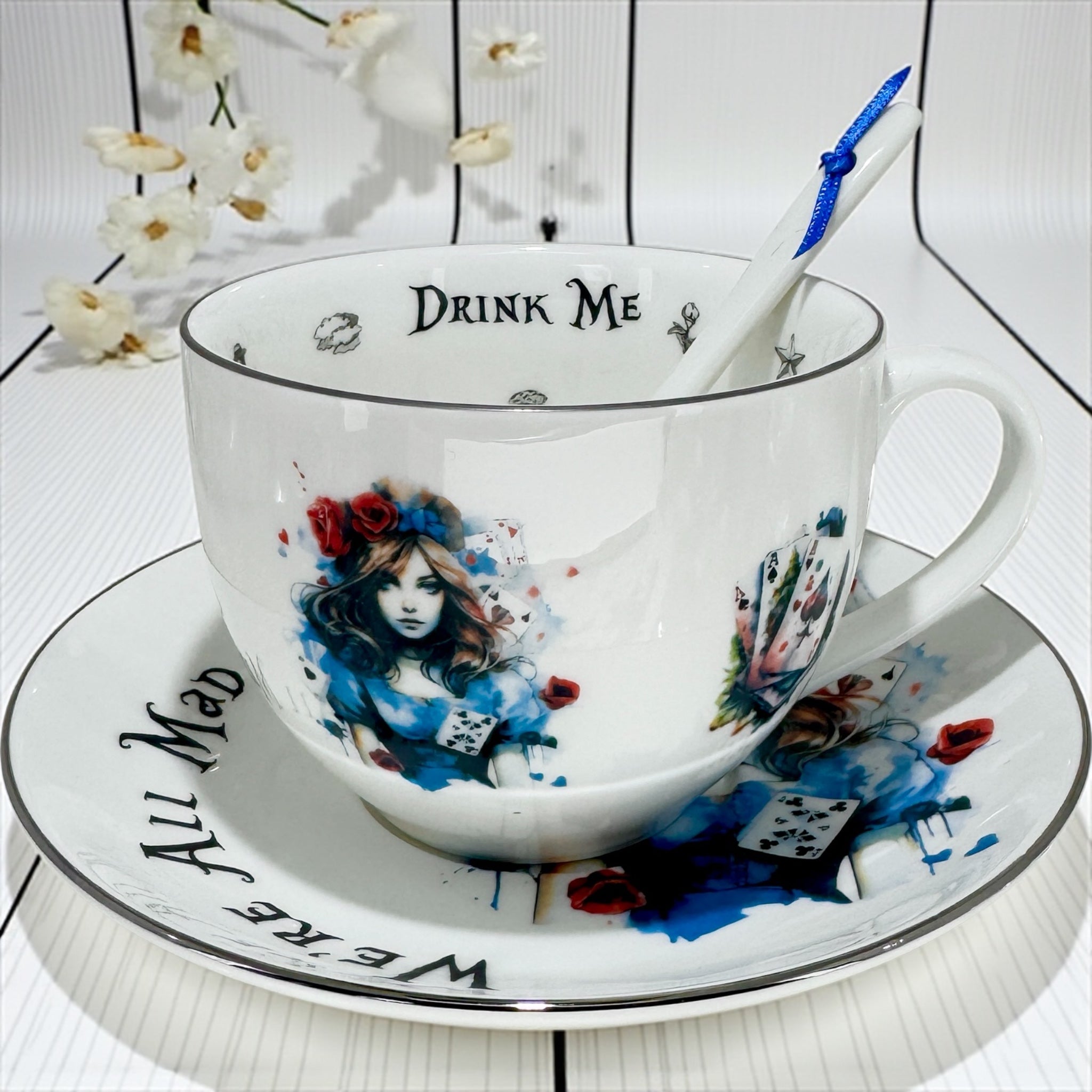 Teacup and saucer with 'Drink Me' text and artistic design on a white background