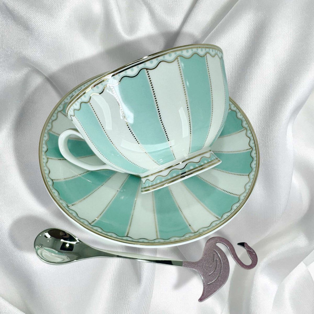 Teacup on saucer with the flamingo spoon next to it featuring turquoise and white vertical stripes