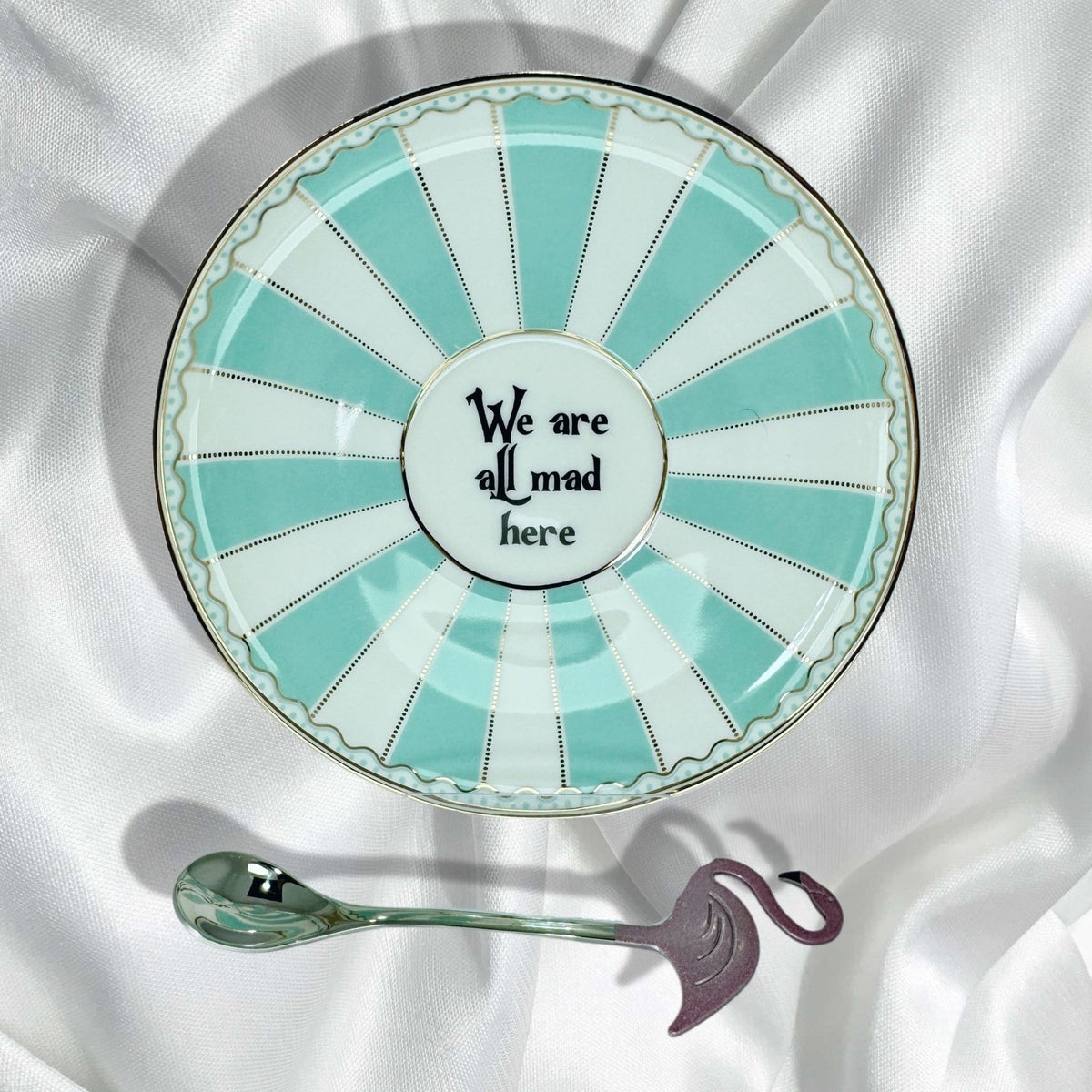 Saucer featuring turquoise and white stripes with gold accents and the quote We are all mad here