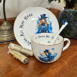 Teacup and saucer with 'Drink Me' text and character design on a wooden surface.