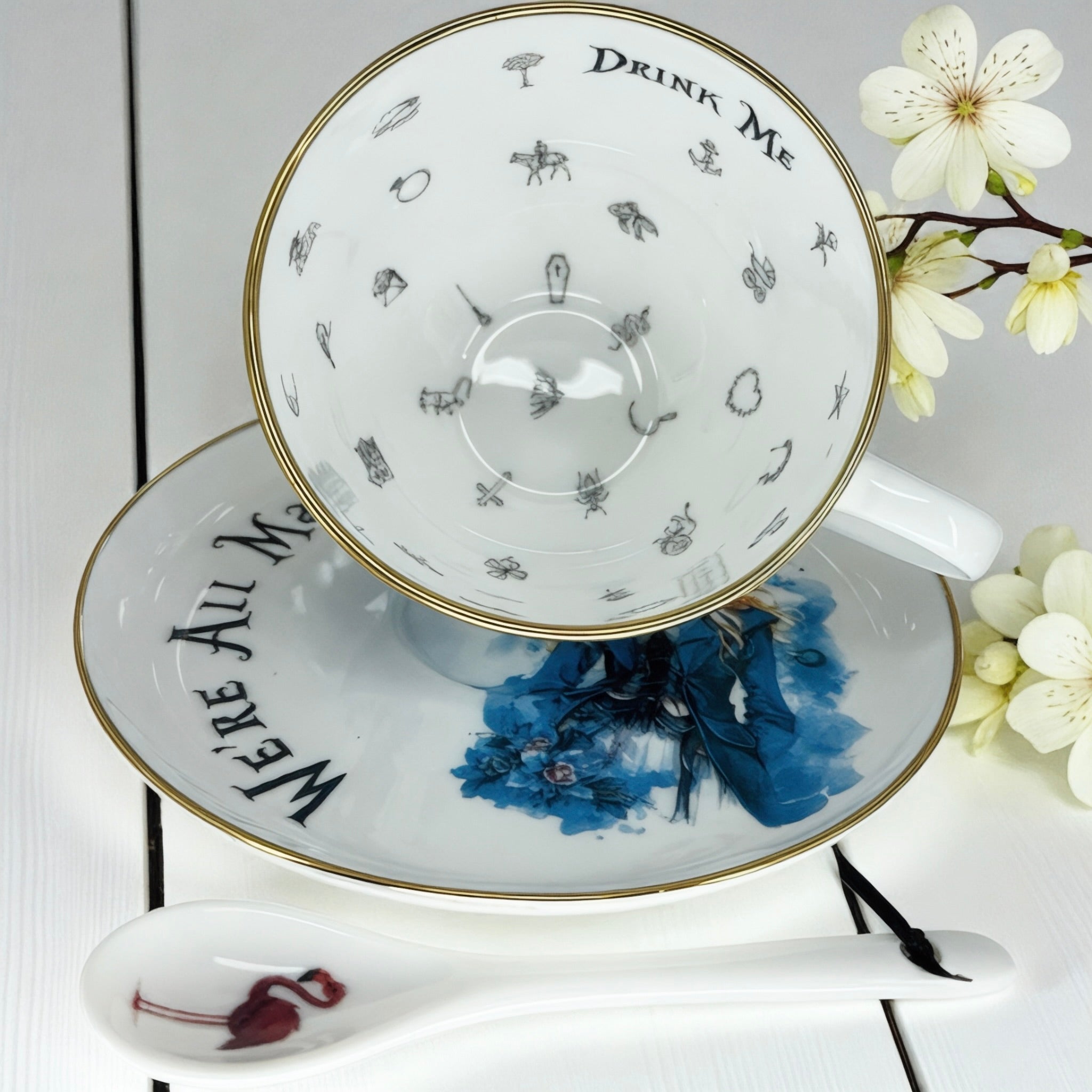 Teacup interior showing 'Drink Me' text and tiny whimsical illustrations of Wonderland icons (anchor, carriage, flowers).