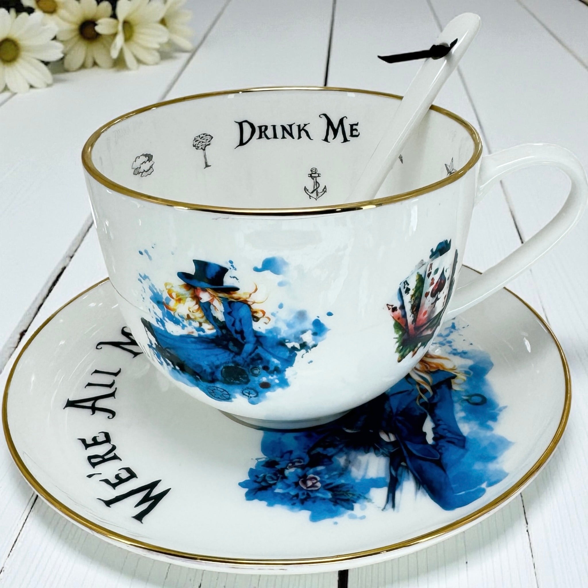 Overhead view of the teacup and saucer, highlighting the 'We're All Mad Here' saucer text and 'Drink Me' teacup interior.