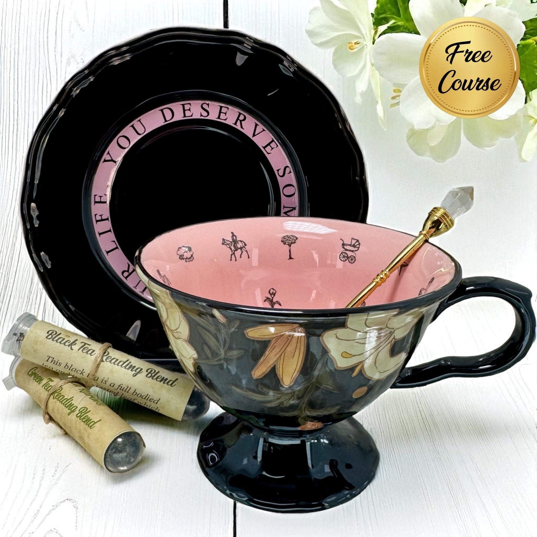 Black and pink teacup set with floral design on a white surface, accompanied by tea and a free course badge. Used for tea leaf reading.