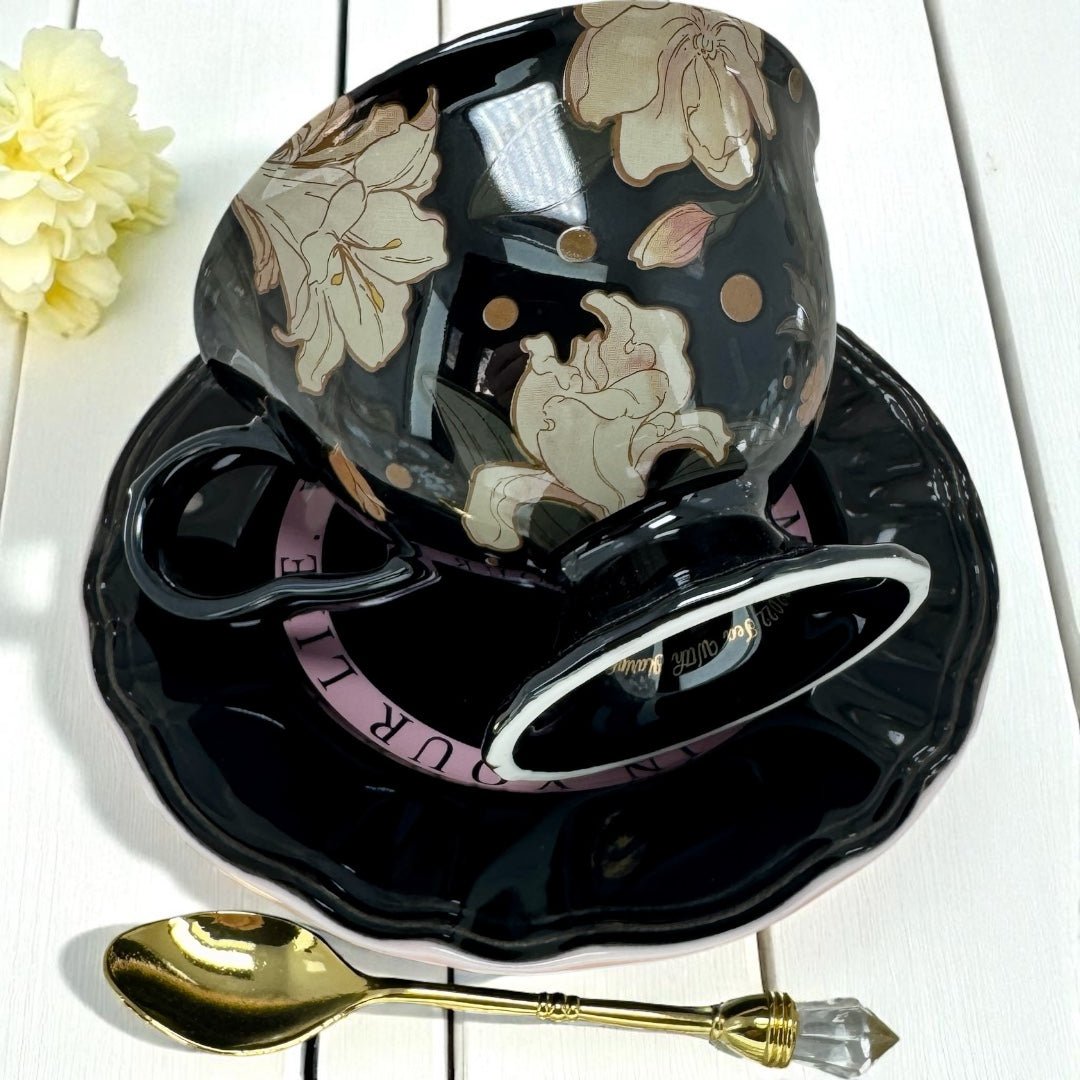 Black floral teacup and saucer set with a gold spoon on a white background
