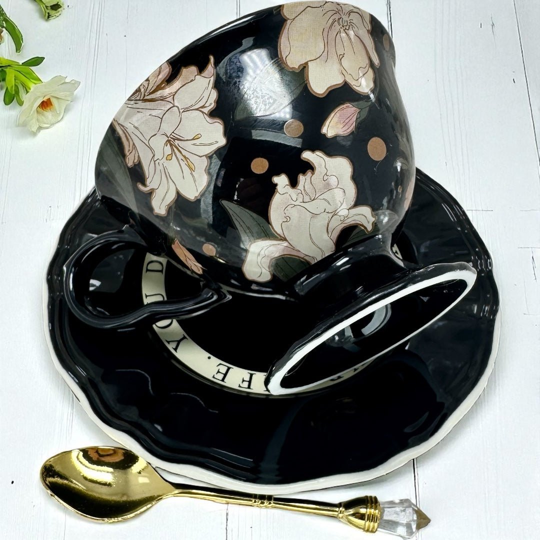 Black floral teacup and saucer set  designed for tea leaf reading with a gold spoon on a white wooden surface.