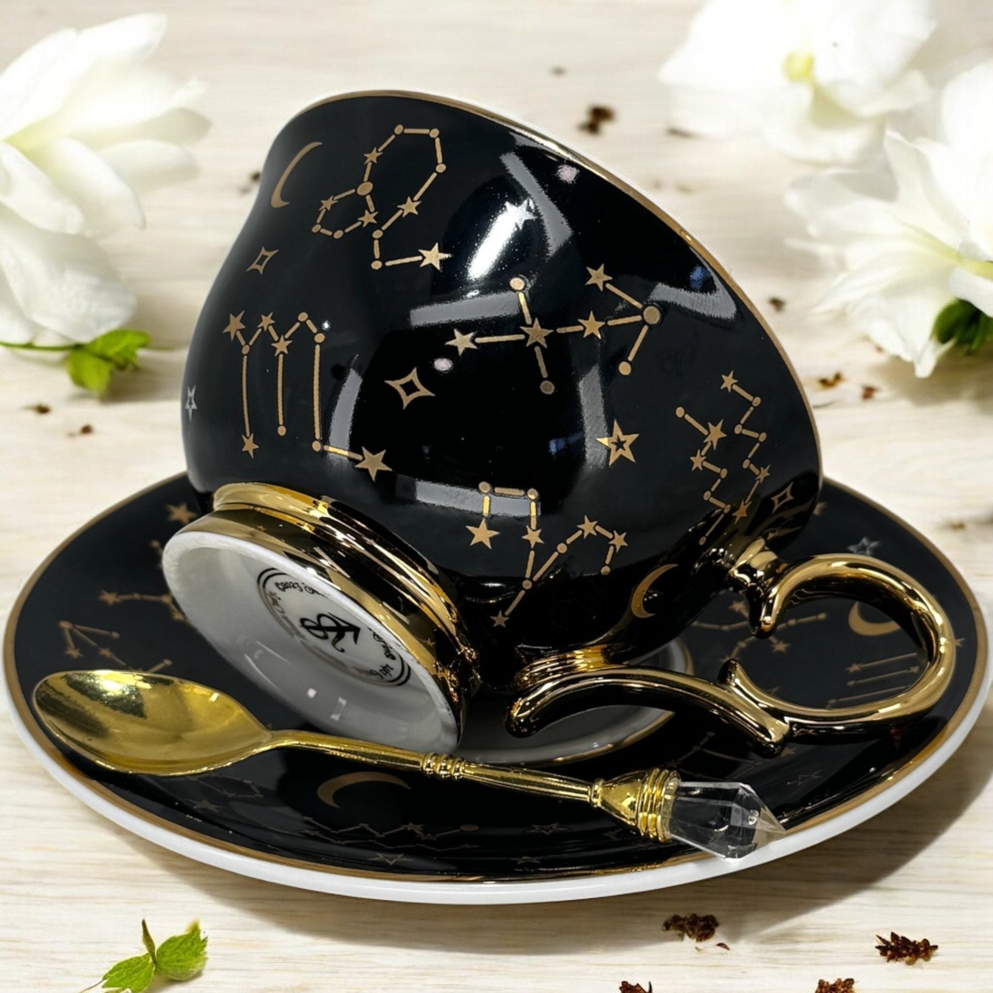 Black tarot-themed teacup and saucer set with mystical tarot symbols inside, accompanied by a symbol guidebook and a gold teaspoon, ideal for daily tea leaf reading and divination