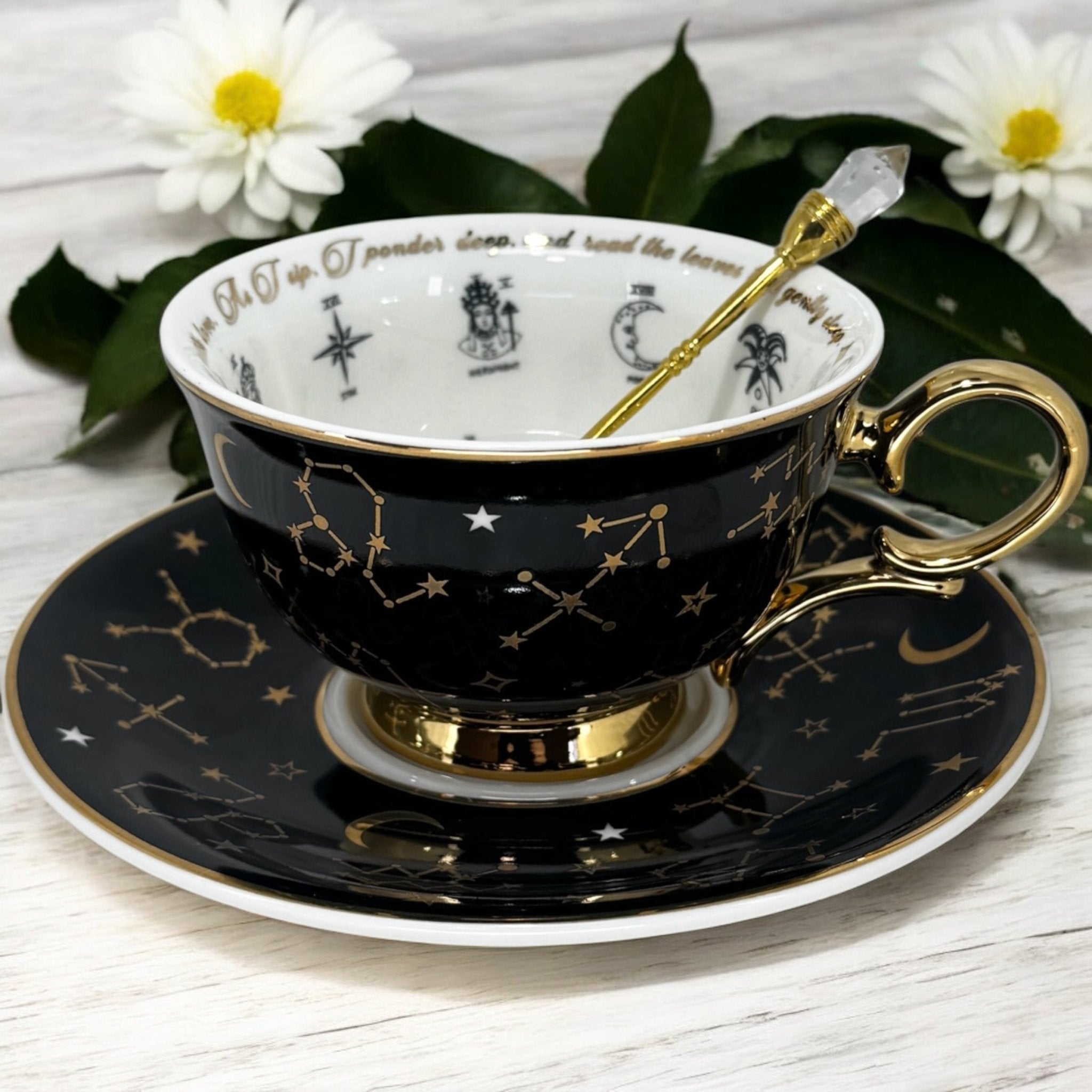 Black tarot-themed teacup and saucer set with mystical tarot symbols inside, accompanied by a symbol guidebook and a gold teaspoon, ideal for daily tea leaf reading and divination