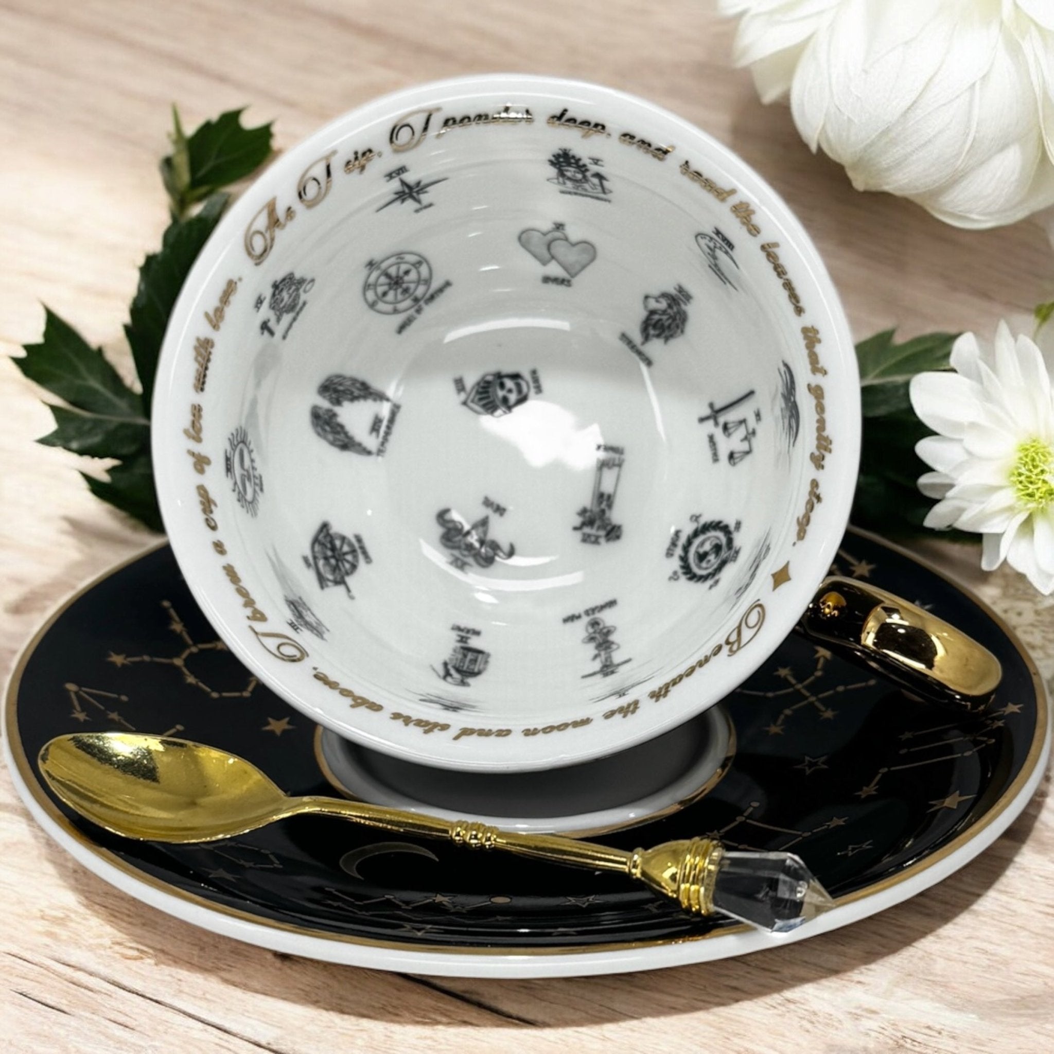 Black tarot-themed teacup and saucer set with mystical tarot symbols inside, accompanied by a symbol guidebook and a gold teaspoon, ideal for daily tea leaf reading and divination
