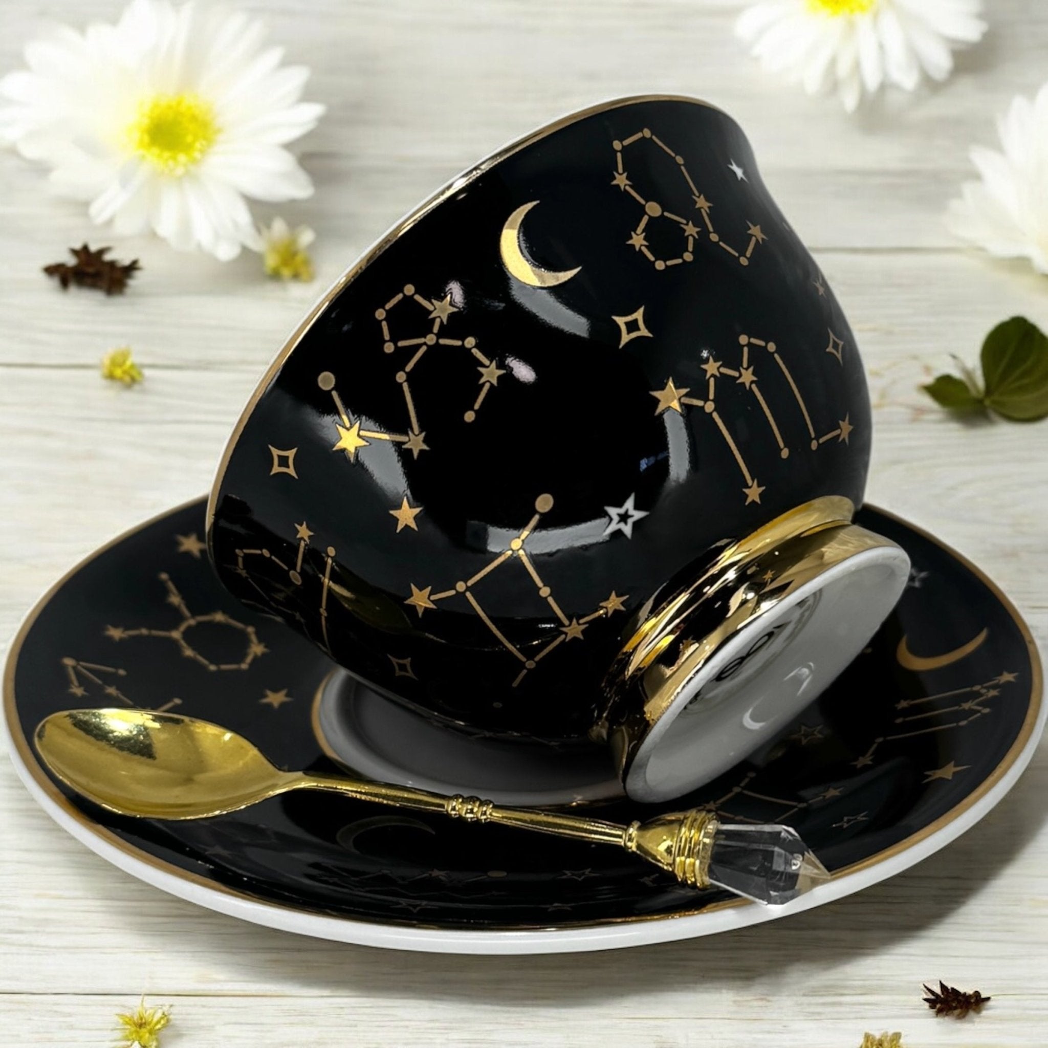 Black tarot-themed teacup and saucer set with mystical tarot symbols inside, accompanied by a symbol guidebook and a gold teaspoon, ideal for daily tea leaf reading and divination