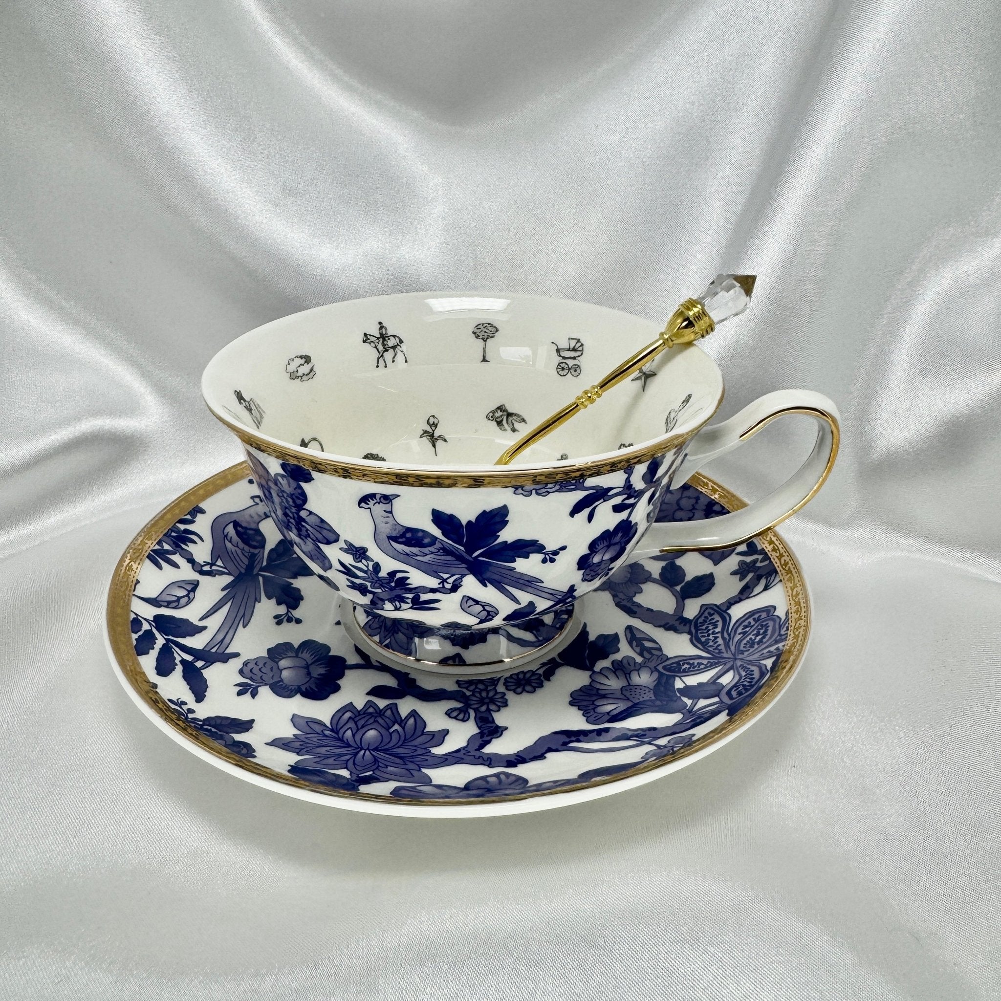 Elegant teacup and saucer in blue and white willow-style design with internal fortune telling motifs and a gold crystal-tipped teaspoon.