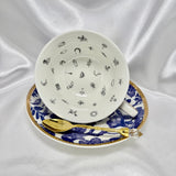 Blue and white teacup and saucer set with gold trim, cup tilted on its side showing tiny black divination symbols inside.