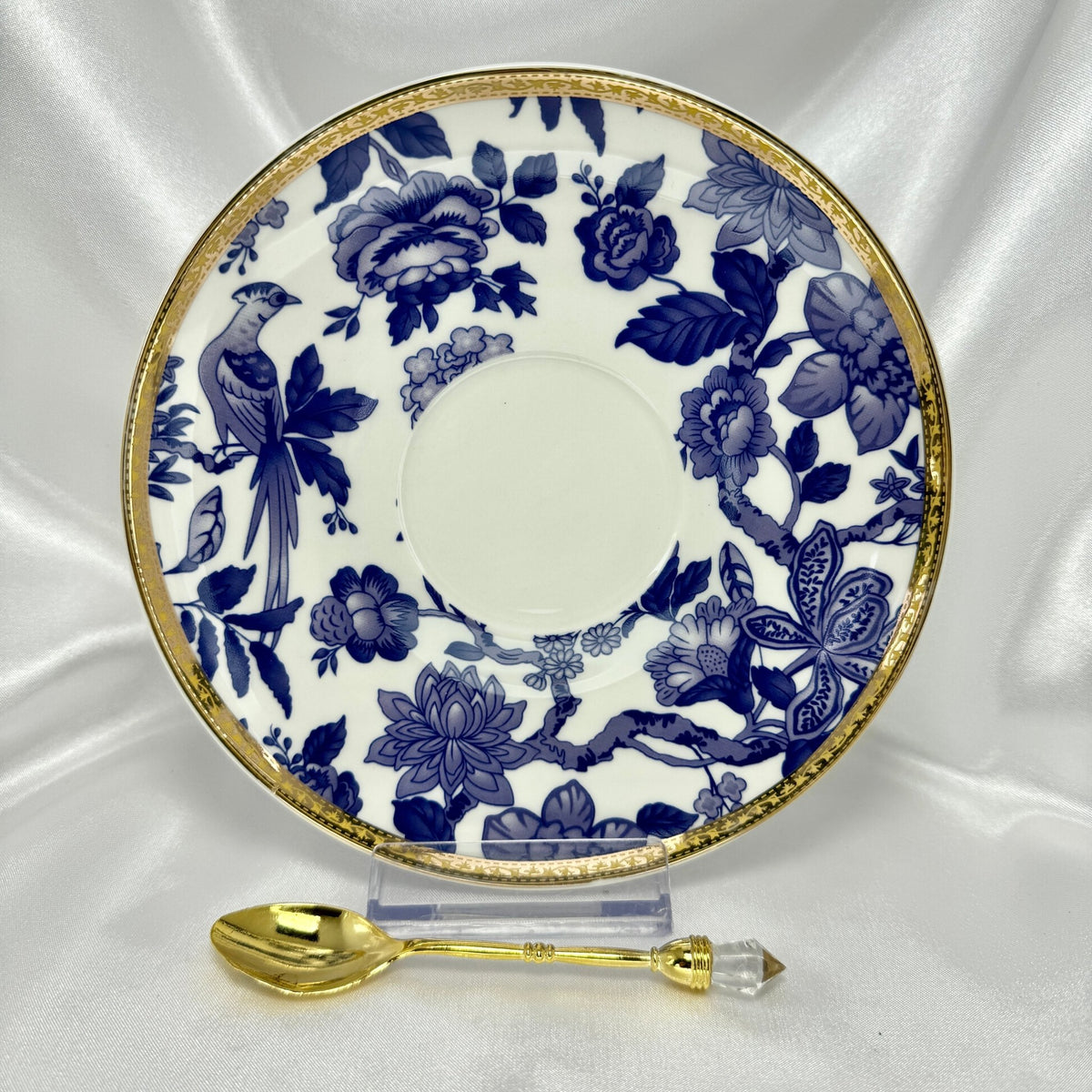 Saucer in blue and white Chinoiserie bird and floral pattern with gold rim, standing upright with a small gold teaspoon.