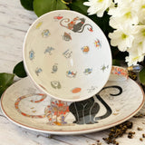Teacup and saucer with cat illustrations on a wooden surface with flowers in the background