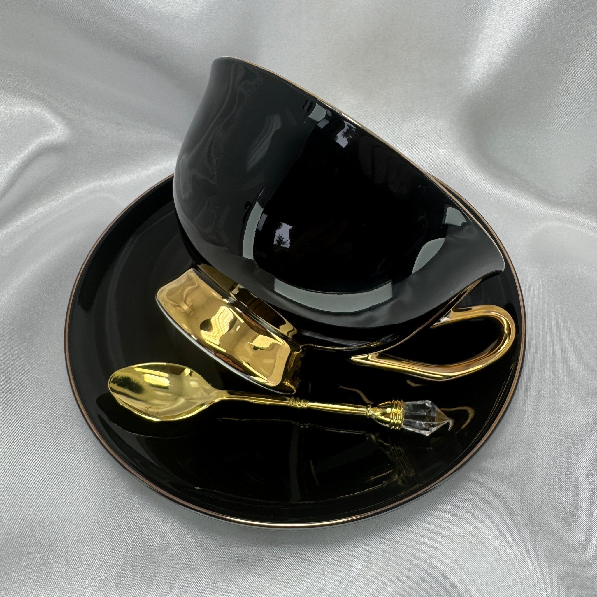 Black teacup and saucer set with gold accents on a gray fabric background