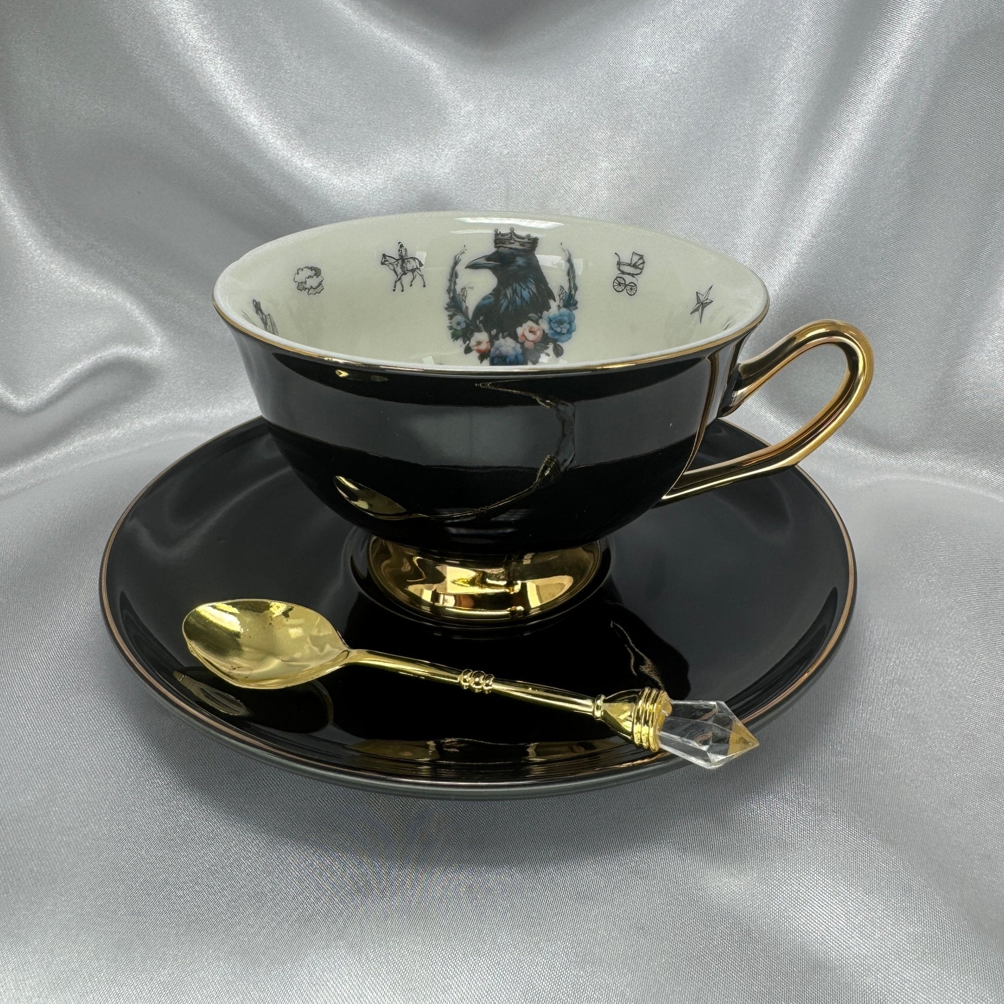 Black teacup and saucer set with gold handle and spoon on a silver fabric background