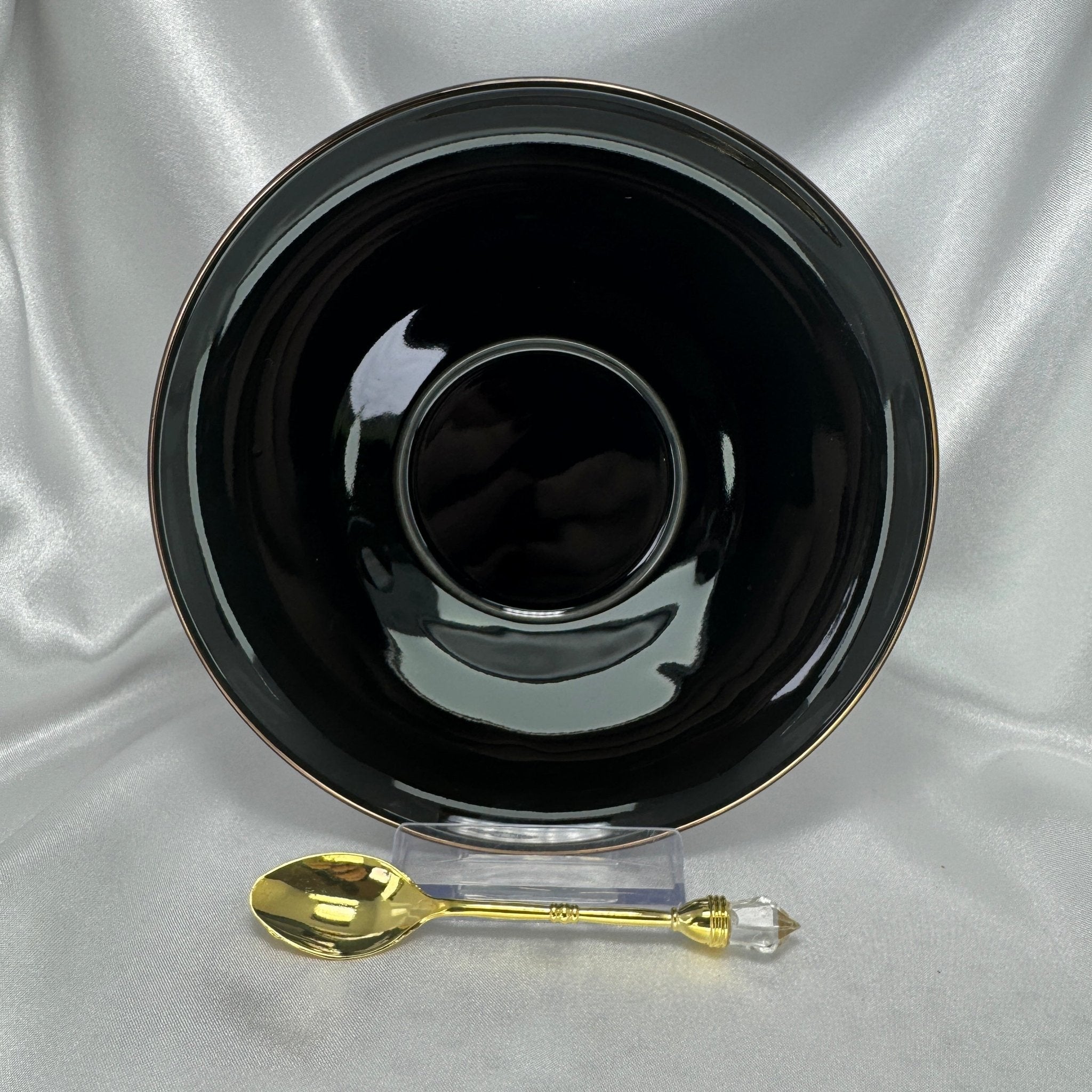 Black bowl with a gold spoon on a silver fabric background