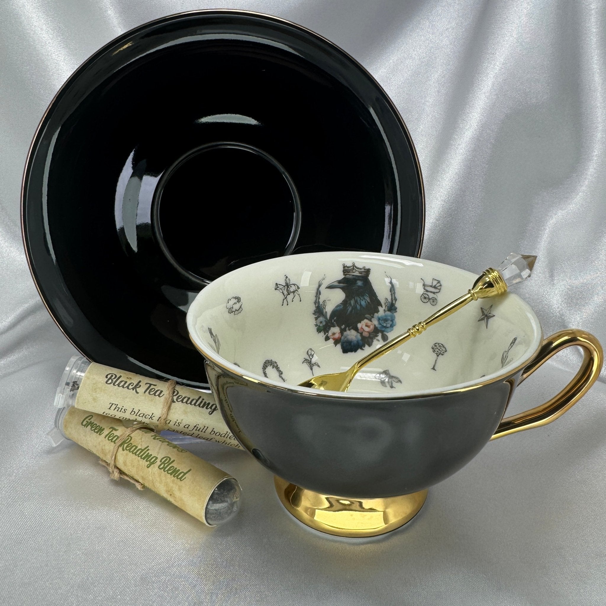 Teacup with gold handle and spoon, black saucer, and tea bags on a silver background