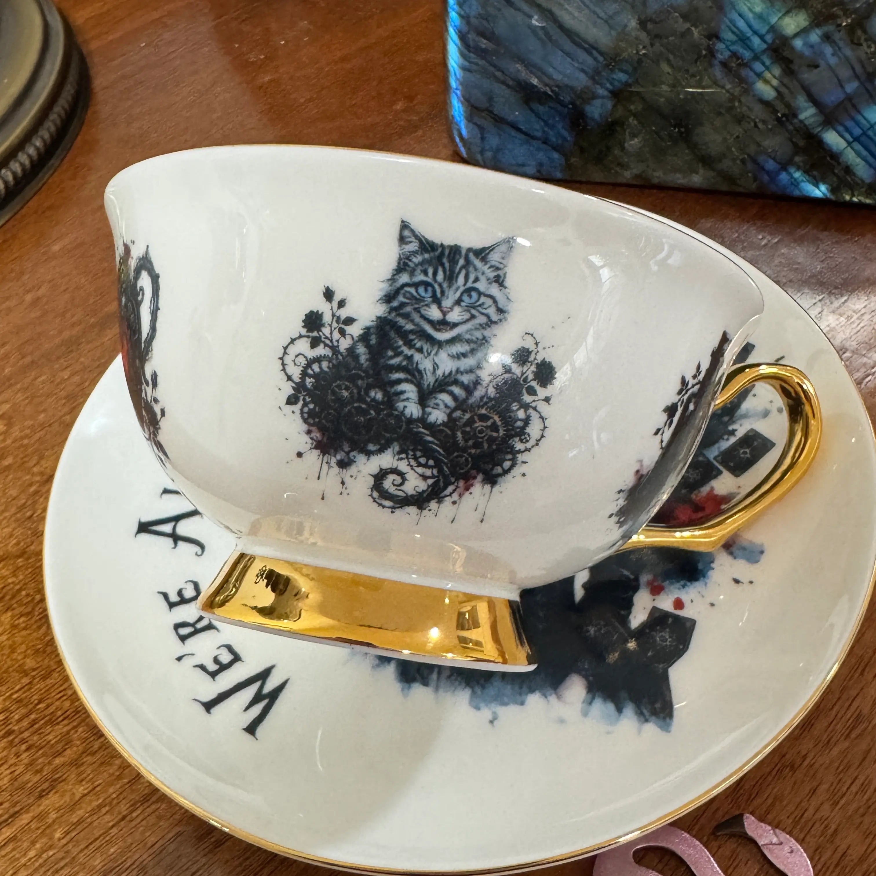 Close-up of the blue-eyed Cheshire Cat among roses and clockwork gears on the gothic Alice teacup
