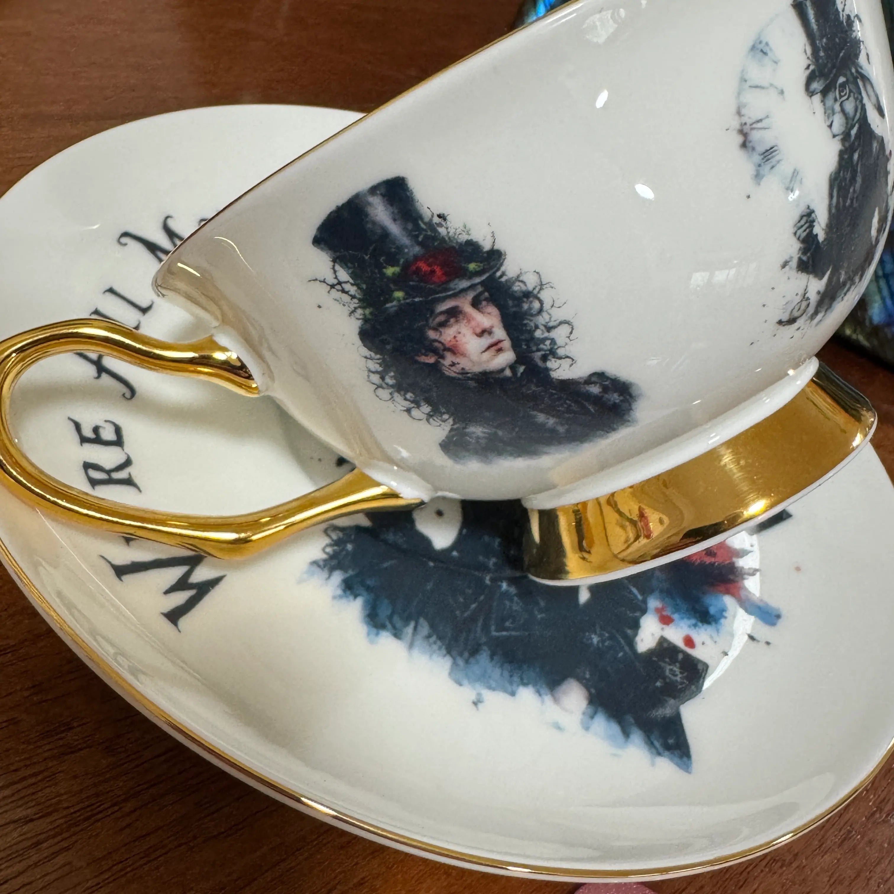 The Hatter in a top hat with a red rose beside the 24ct gold handle of the gothic Alice teacup