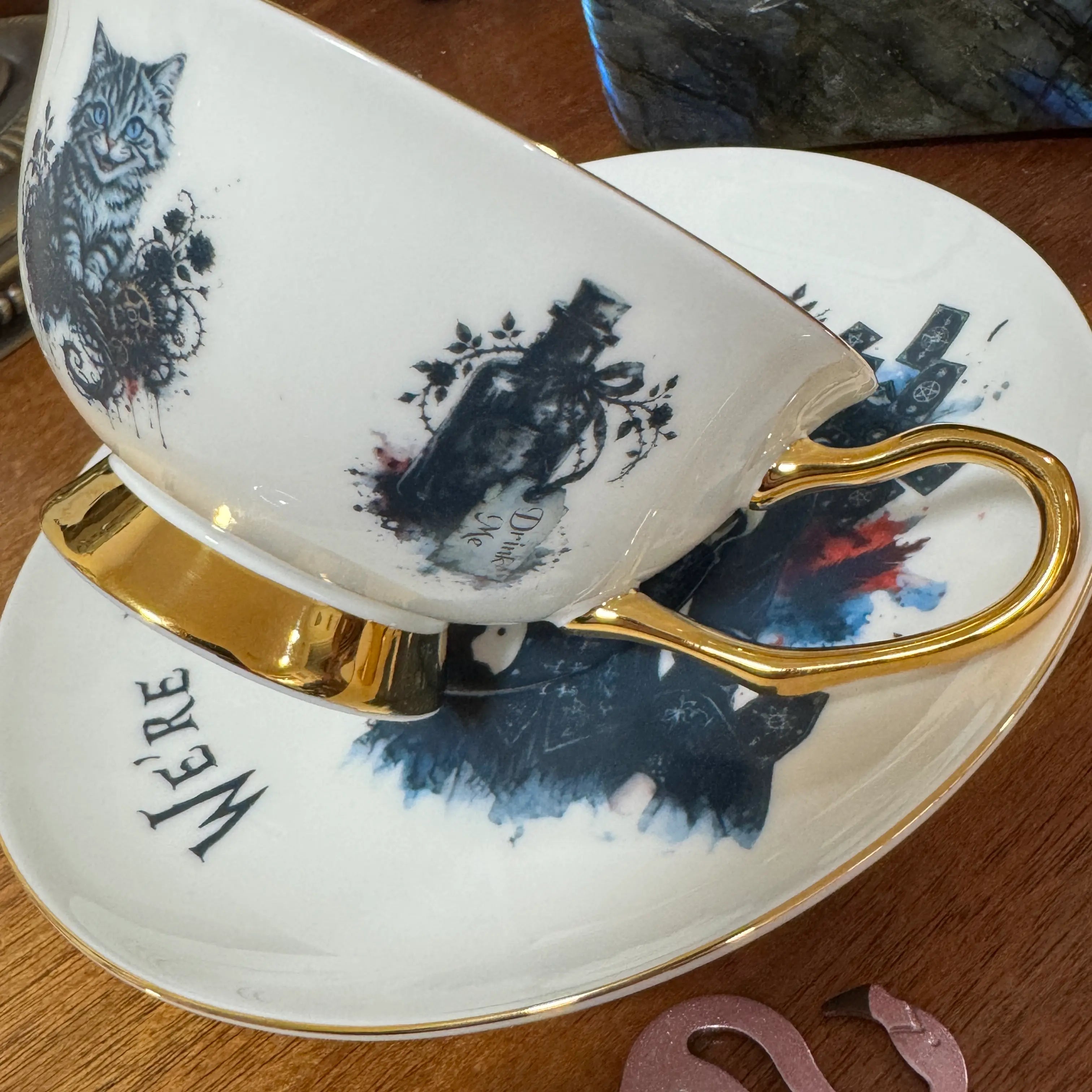 Drink Me bottle artwork with roses beside the Cheshire Cat and 24ct gold handle of the gothic Alice teacup