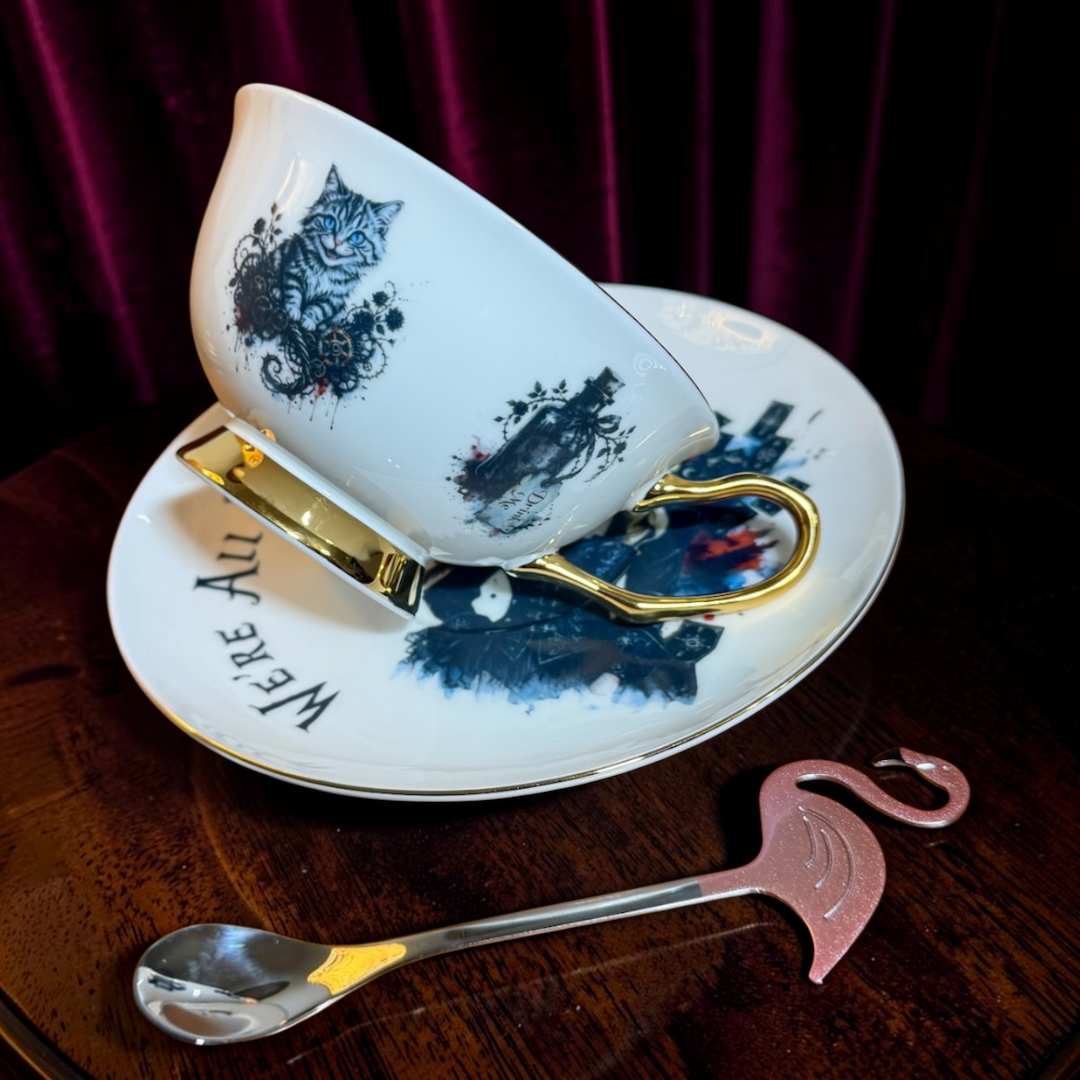 Tilted gothic Alice teacup showing blue-eyed Cheshire Cat and Drink Me bottle artwork