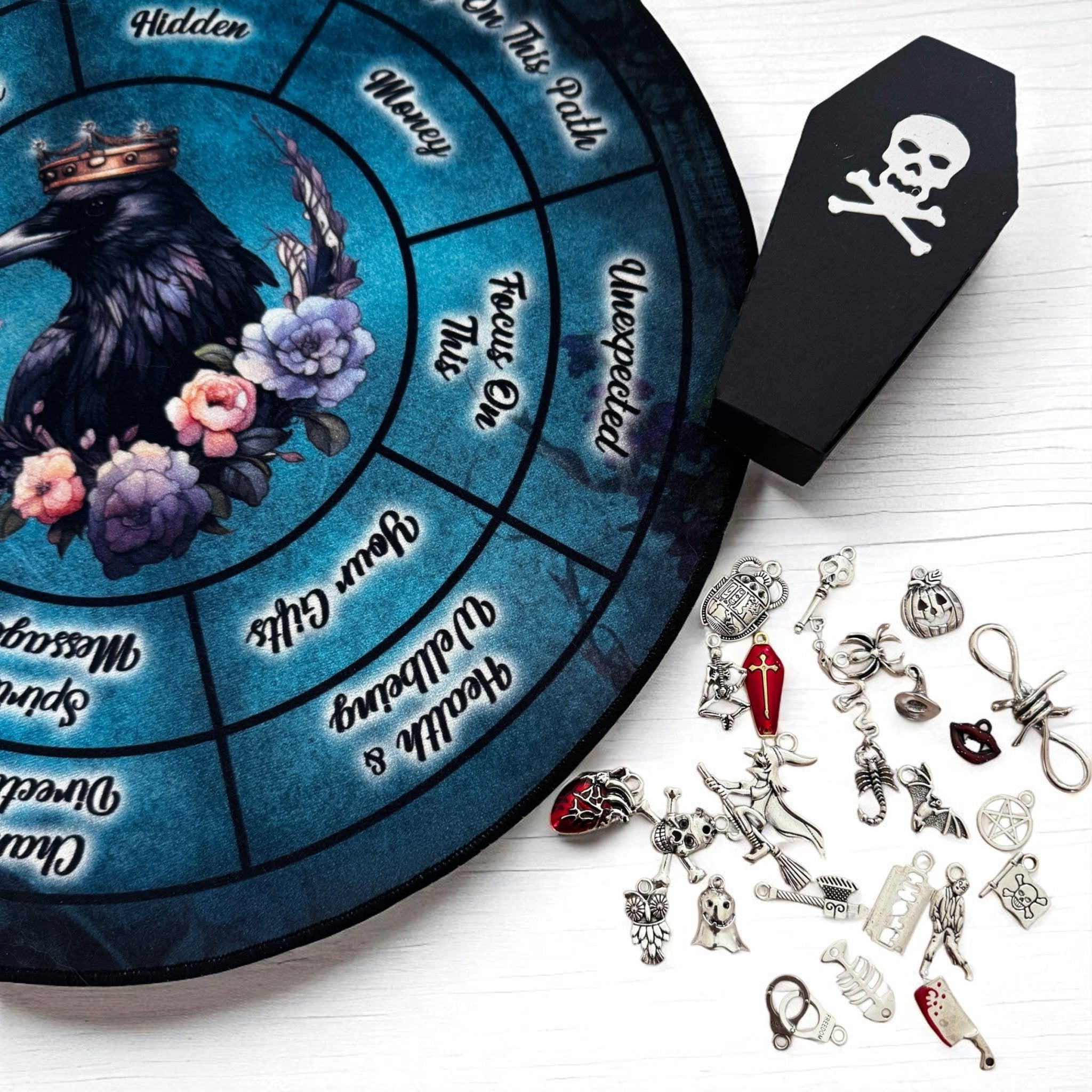 Velvet charm casting mat with a raven and flowers, surrounded by Halloween-themed charms on a white surface.