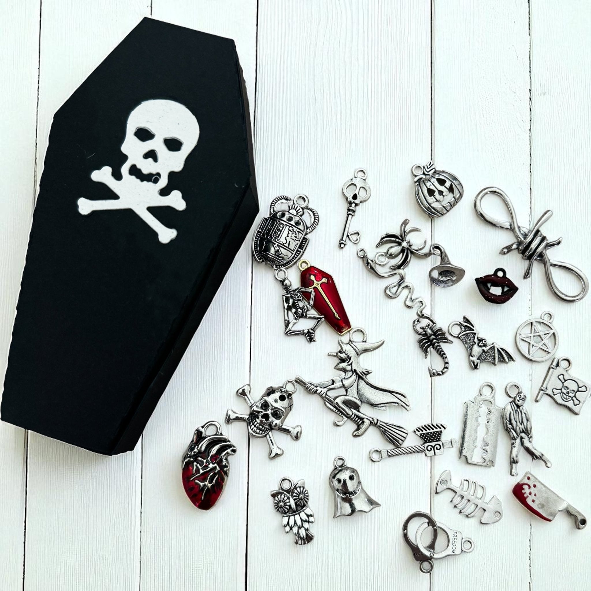 Black coffin-shaped box with skull design on a white wooden surface, surrounded by various Halloween-themed charms.