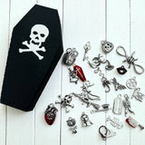 Black coffin-shaped box with skull design on a white wooden surface, surrounded by various Halloween-themed charms.