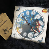 A porcelain tile with a black plastic spinner on it, featuring Halloween themed decorations, accompanied by a box of charms.