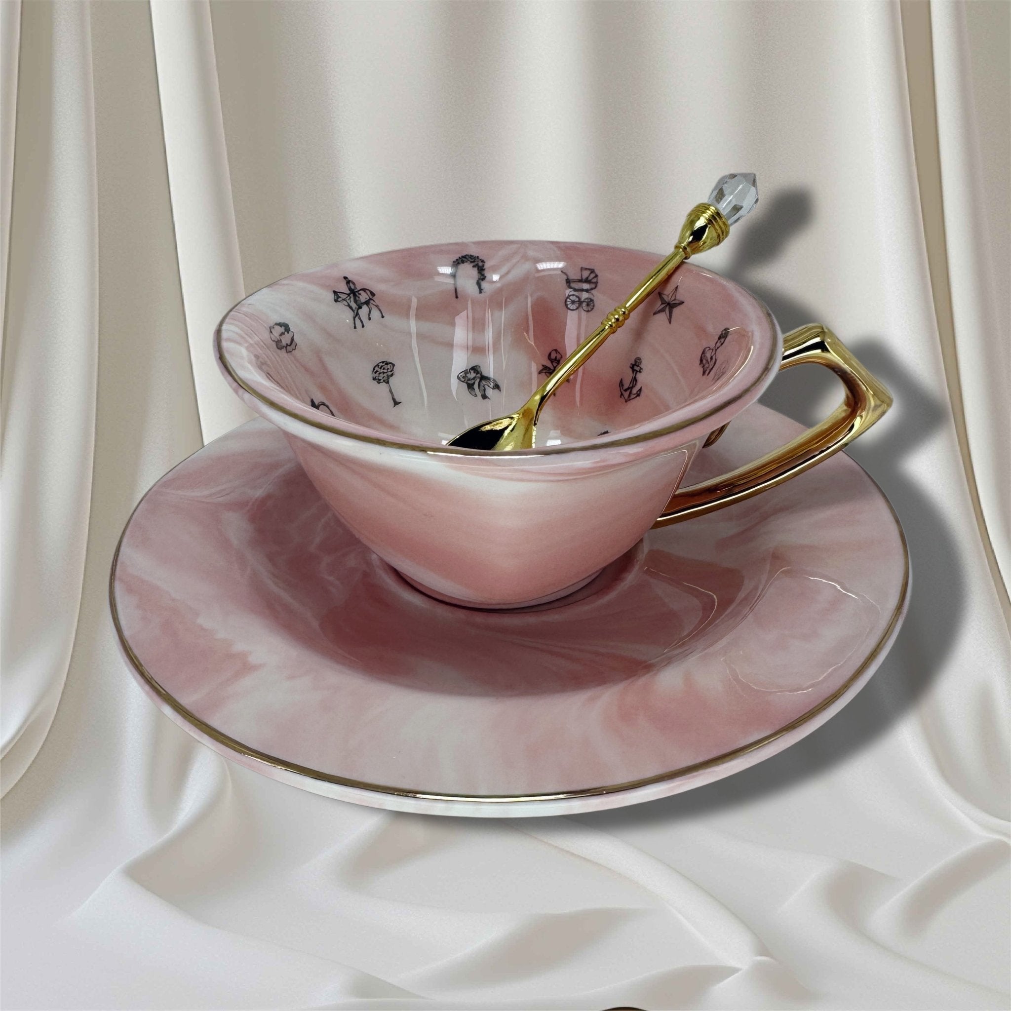 Pink teacup with gold handle and spoon on a matching saucer against a white curtain background