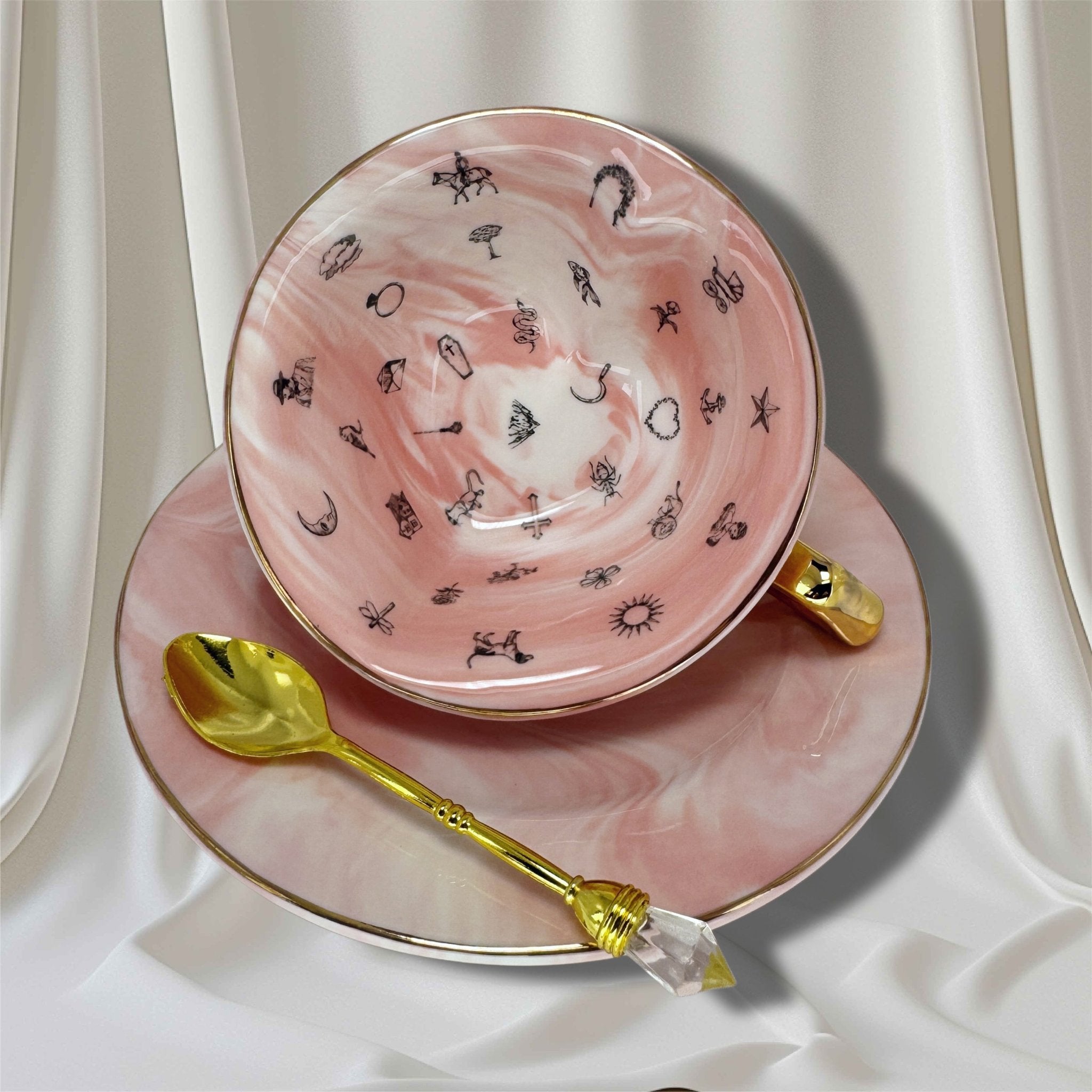Close-up of the interior of the teacup on its side, revealing black fortune-telling symbols against the pink and white marbled surface.