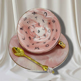 Close-up of the interior of the teacup on its side, revealing black fortune-telling symbols against the pink and white marbled surface.