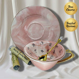 Pink marble-effect teacup and saucer set with a gold spoon and two 'Black Tea Reading Blend' sample tubes on white satin
