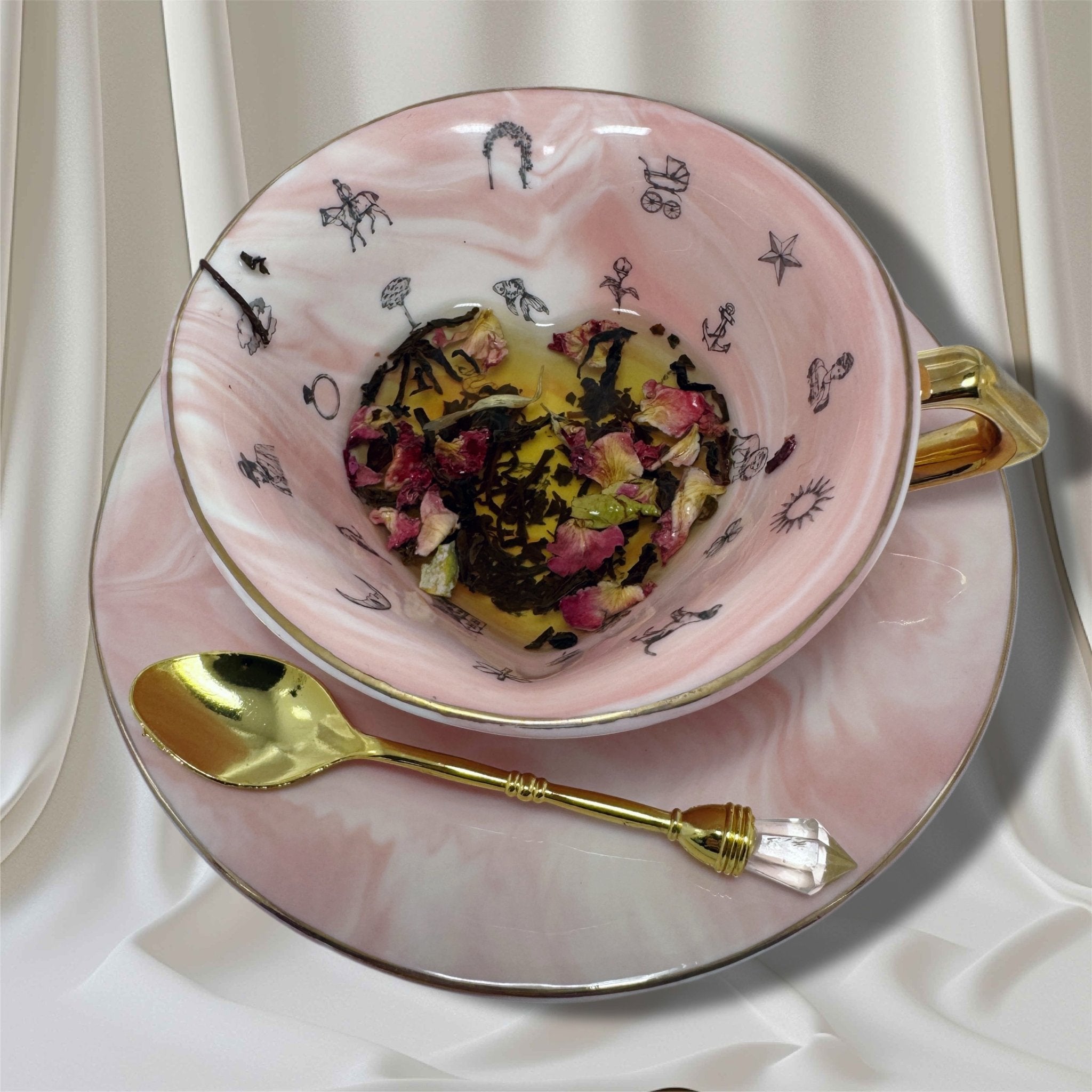 Pink and white marbled teacup and saucer set with a gold handle and rim, featuring internal black symbols for tasseography or tea leaf reading.