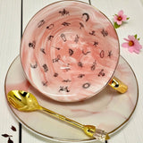 Video showcasing the pink marble-effect teacup and saucer set, rotating to display the gold handle and the full collection of black fortune-telling symbols inside the cup.