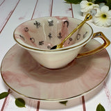 White teacup on its side, showing the internal black line drawings of fortune telling symbols like a crescent moon, dog, house, and ring.