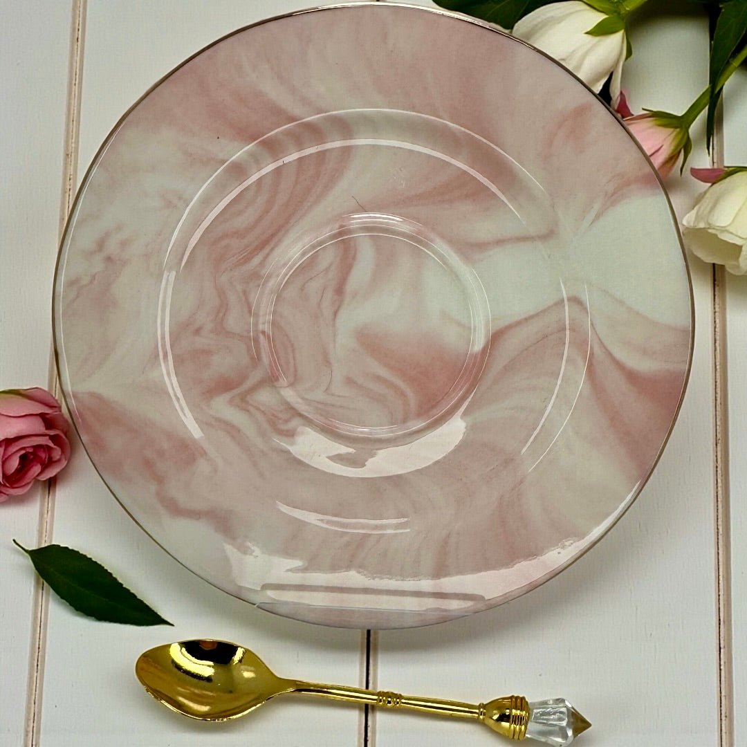 Close-up of pink marble effect teacup saucer with gold rim and matching gold teaspoon with clear crystal handle.