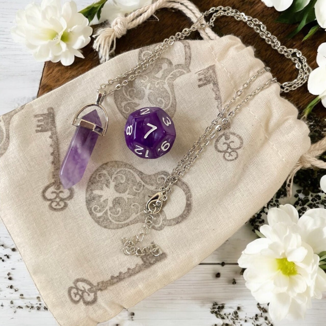 Purple die with silver chain and amethyst on a decorative cloth with flowers