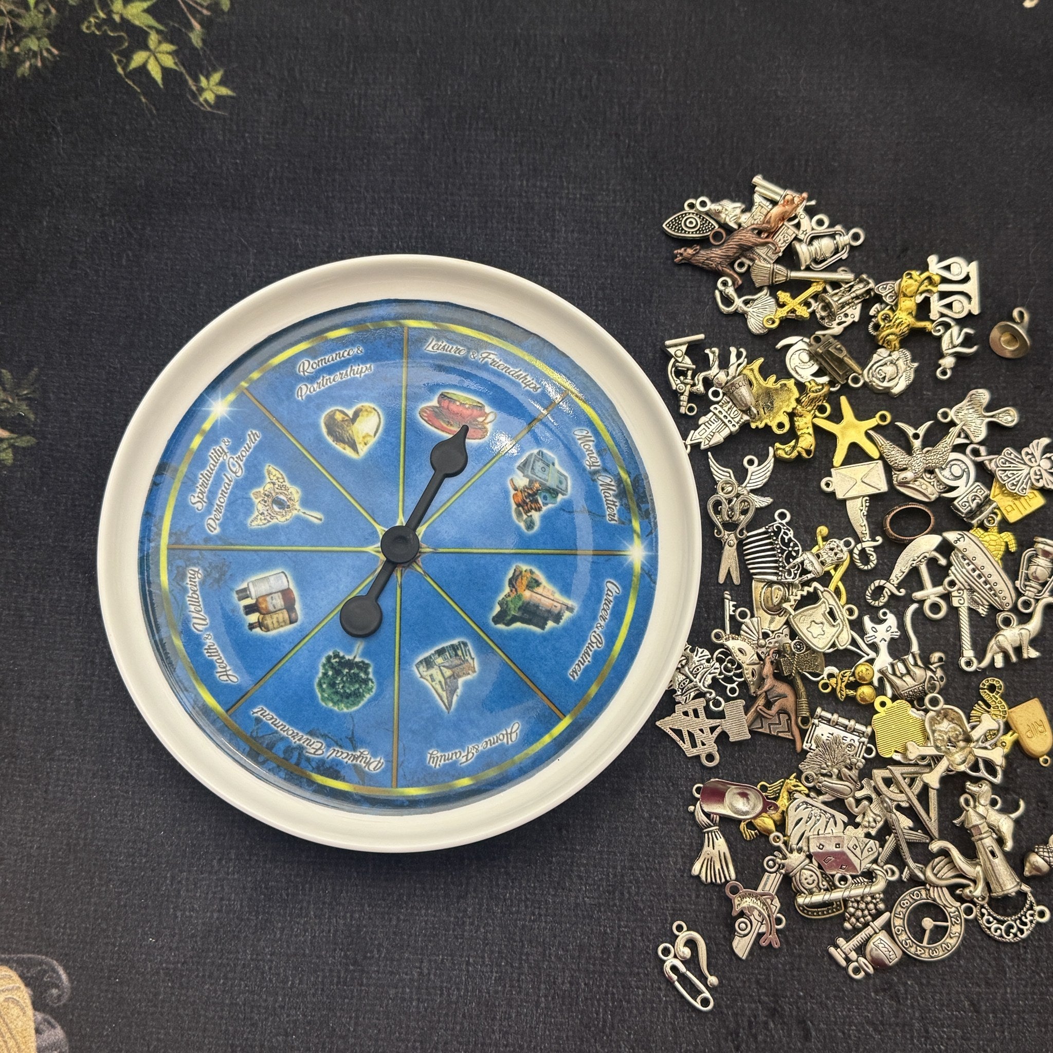 Life Wheel porcelain plate spinner with black spinner and a pile of silver and gold divination charms for charm casting