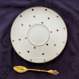 White plate with gold polka dots and a gold spoon on a purple fabric background