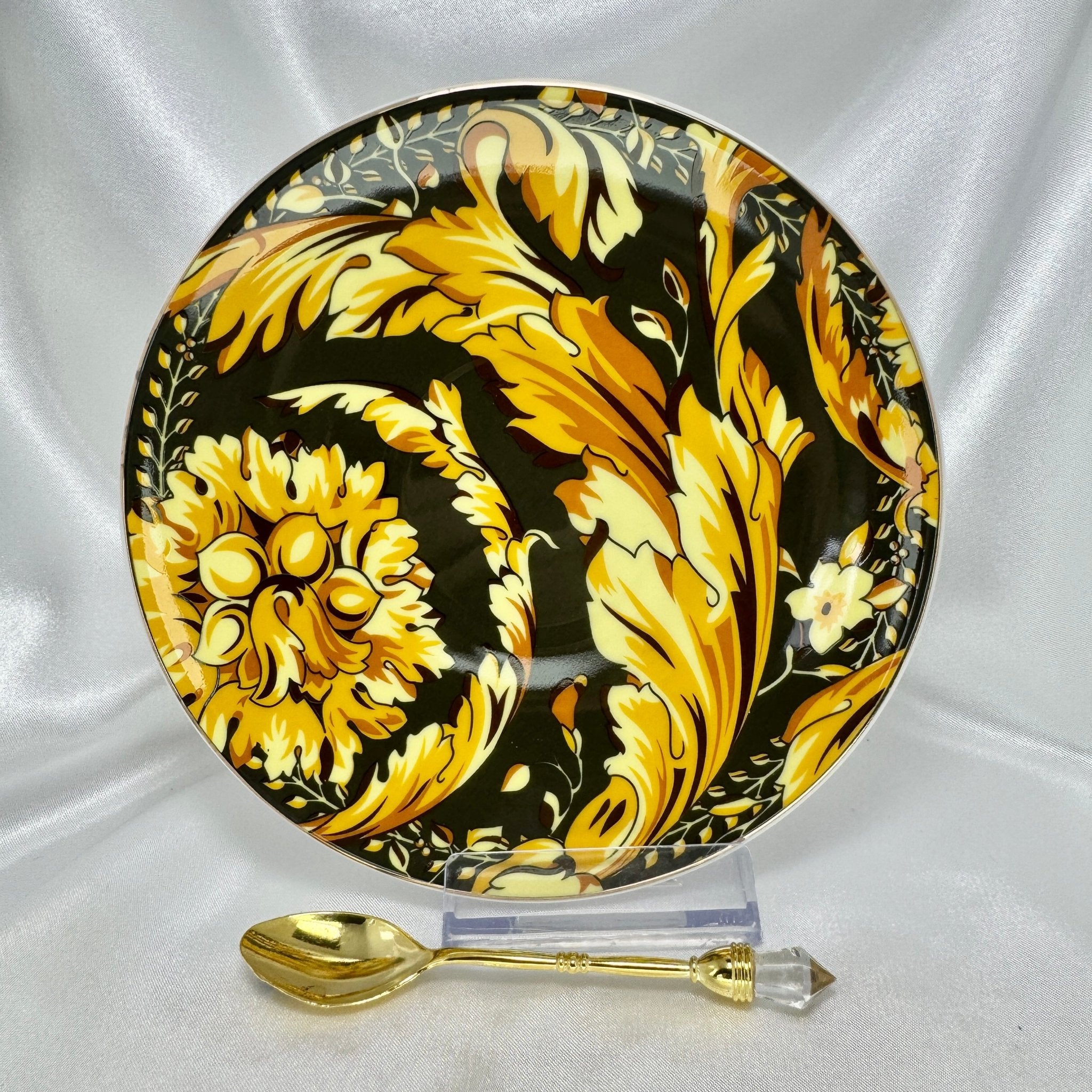 Close-up of black and gold baroque floral patterned saucer with matching gold teaspoon resting in front
