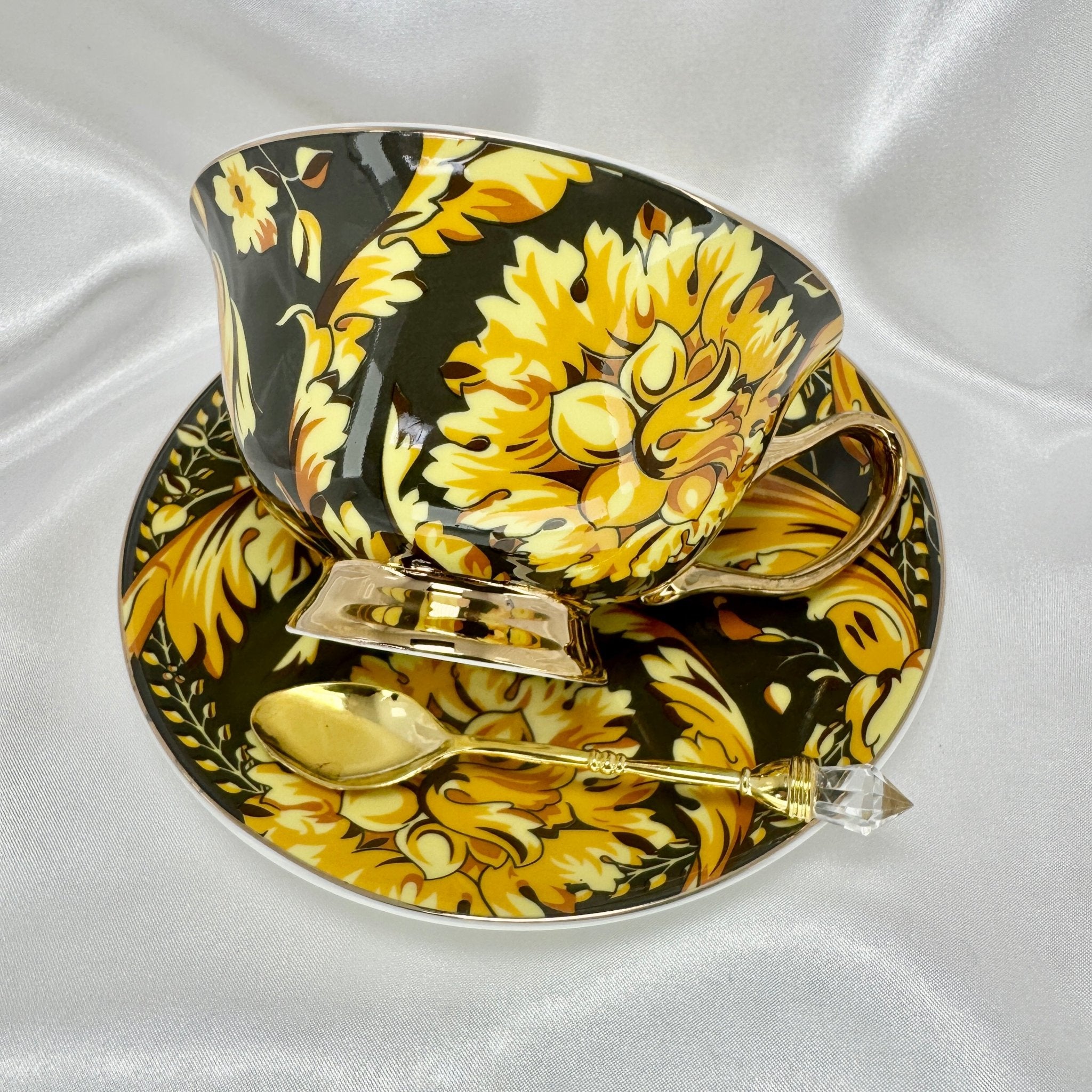 Right side view of the black and gold teacup and saucer set with a gold handle and spoon, resting on white satin